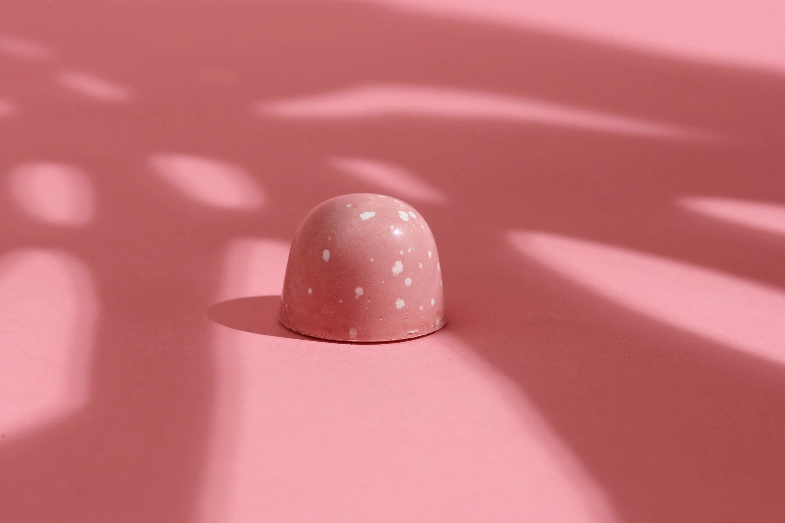 A pink, speckled half-sphere object casting shadows on a pink surface with light reflections creating a pattern.