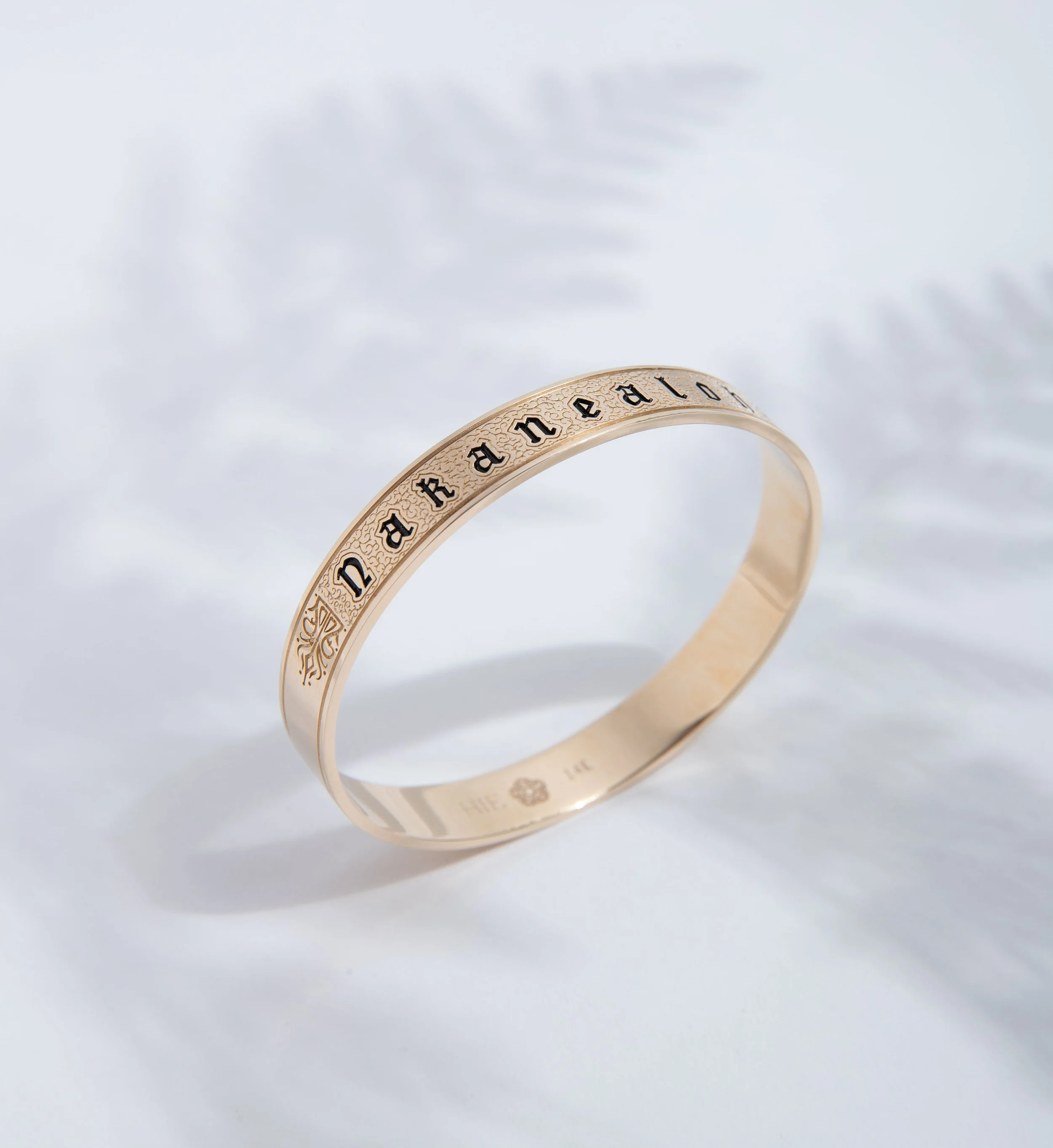 A gold ring with the word 'fearless' engraved around it, placed on a white surface with soft shadows and faint leaf patterns in the background.