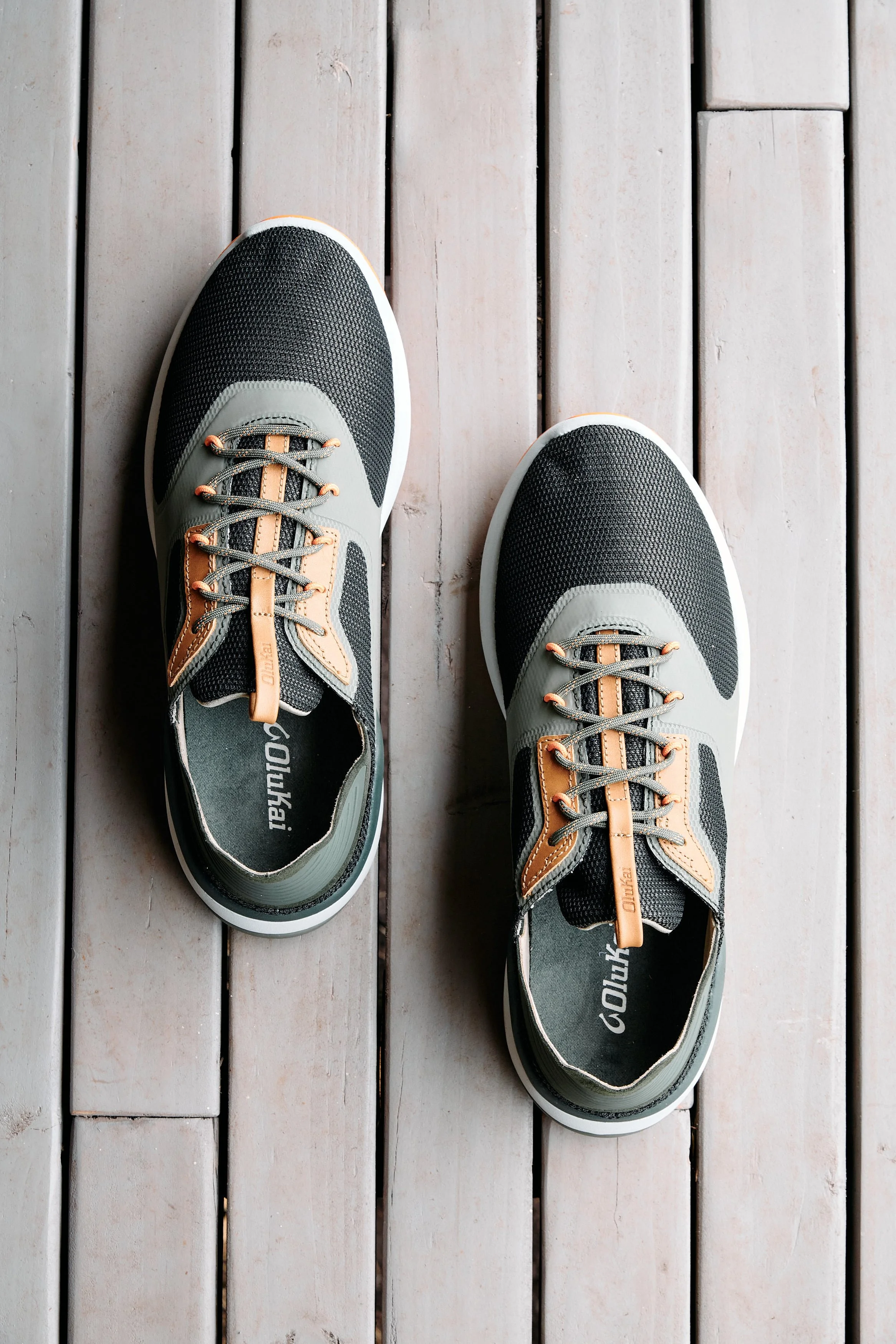 Pair of modern black and gray athletic shoes with orange accents on a light wooden floor.
