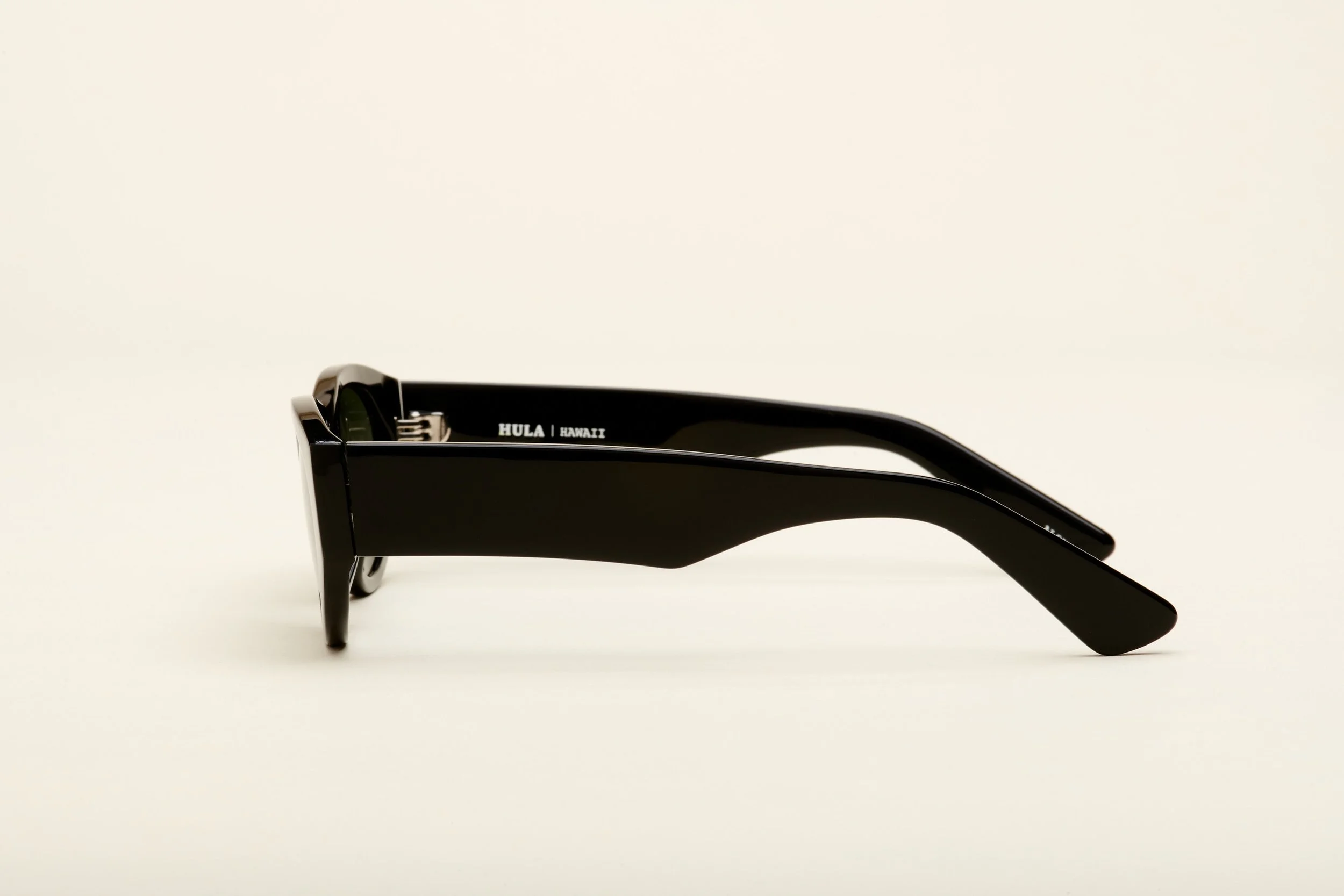 Side view of black sunglasses with text "HULA | HAWAII" on the inside of the arm, on a plain white background.