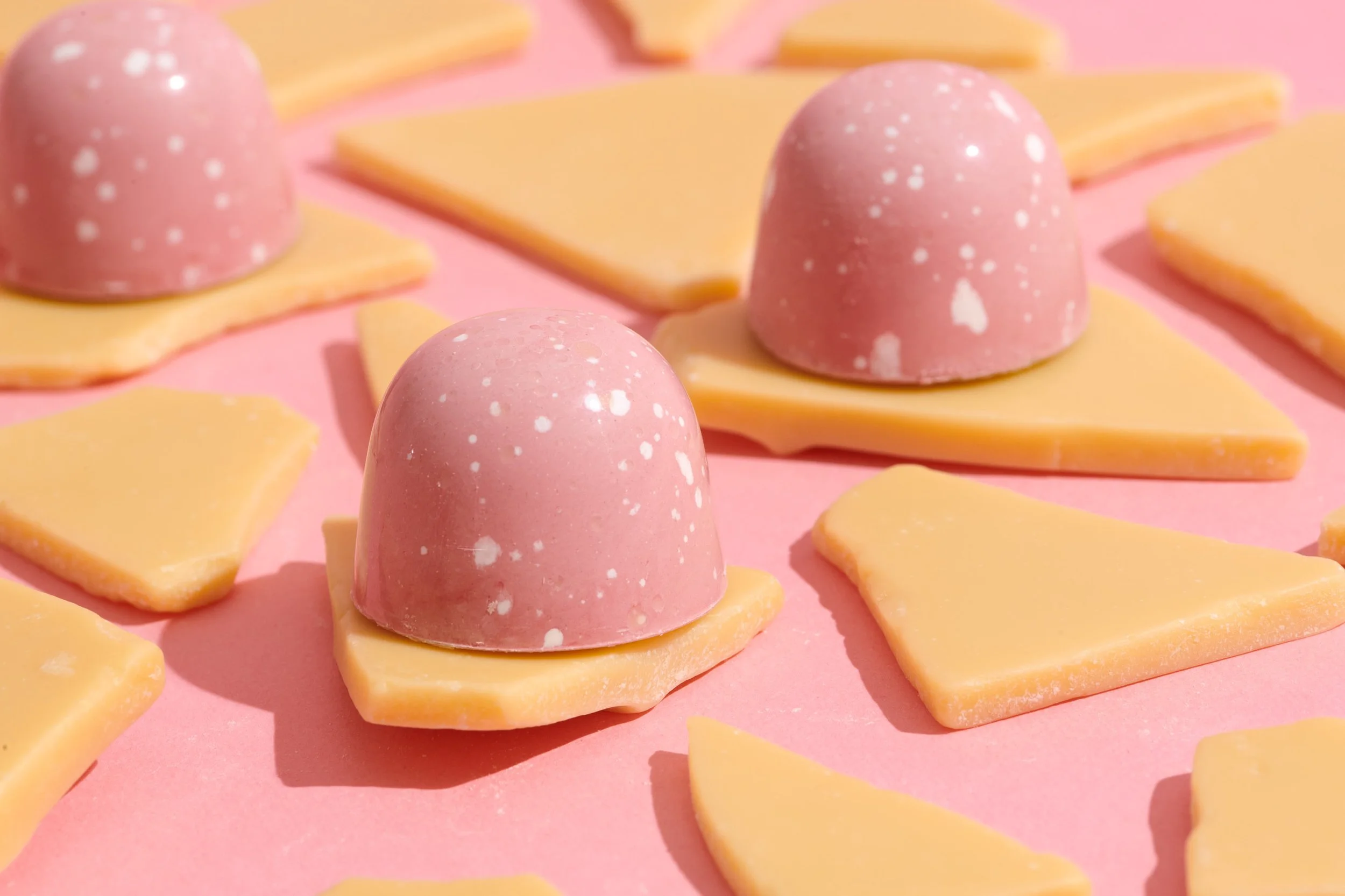 Pink and yellow cheese and chocolate candies on pink background.