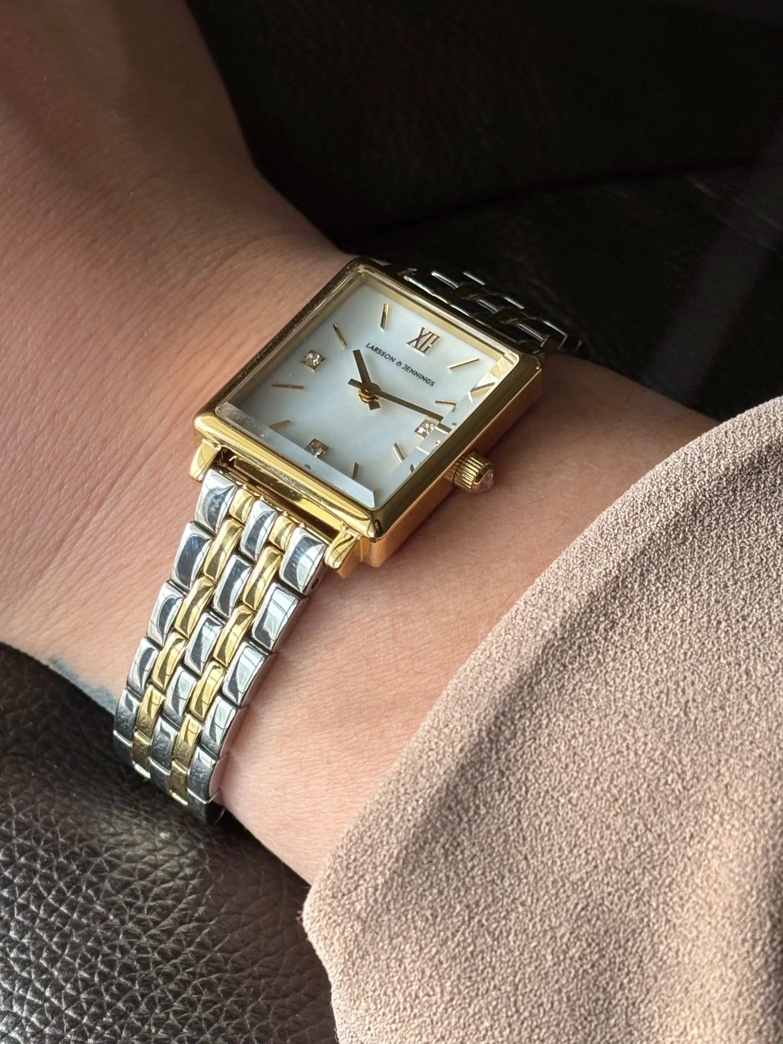 A wrist wearing a rectangular gold and silver two-tone watch with a white face and gold Roman numeral and diamond hour markers.