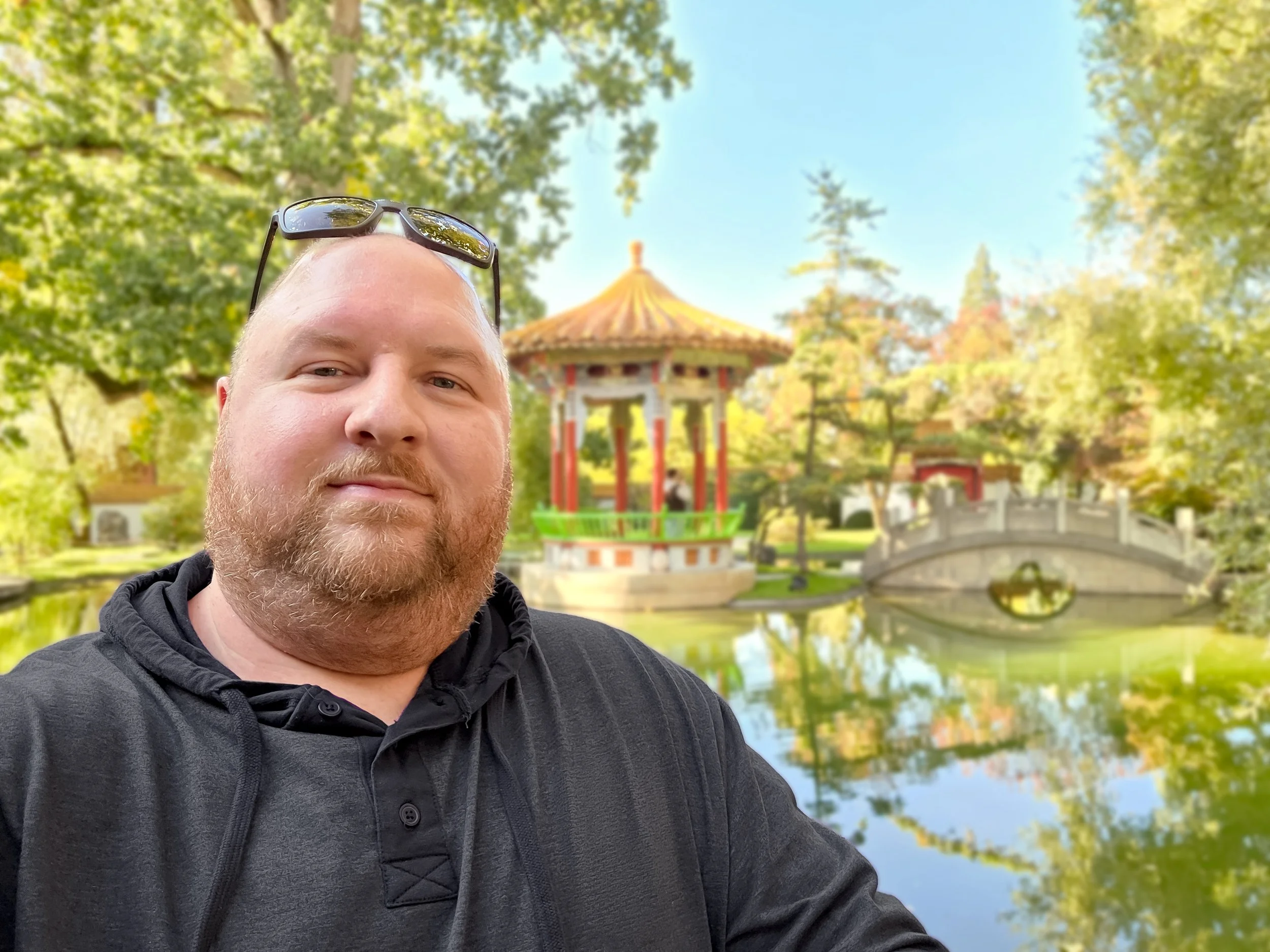 Portrait of Ryan Merritt standing in a zen garden with a pond in the background, wearing a dark neutral hoodie.