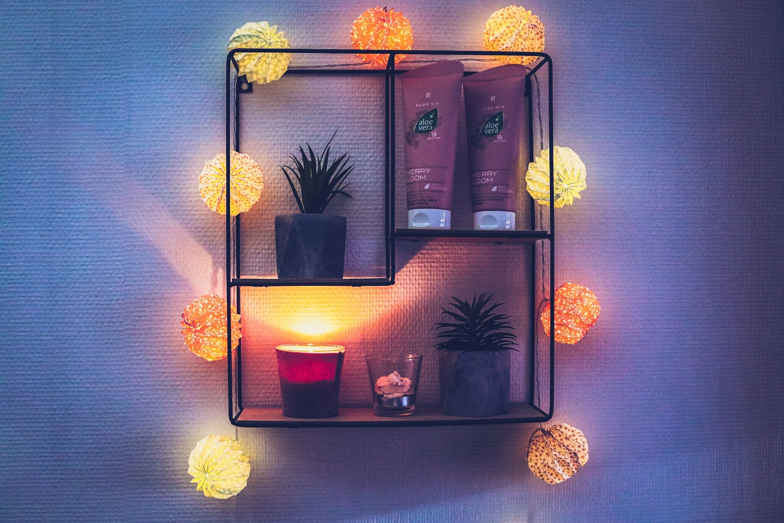Wandregal mit Potted Plants, Lotionflaschen und Kerzen, umgeben von farbigen Papierlaternenlichtern in Innenraum