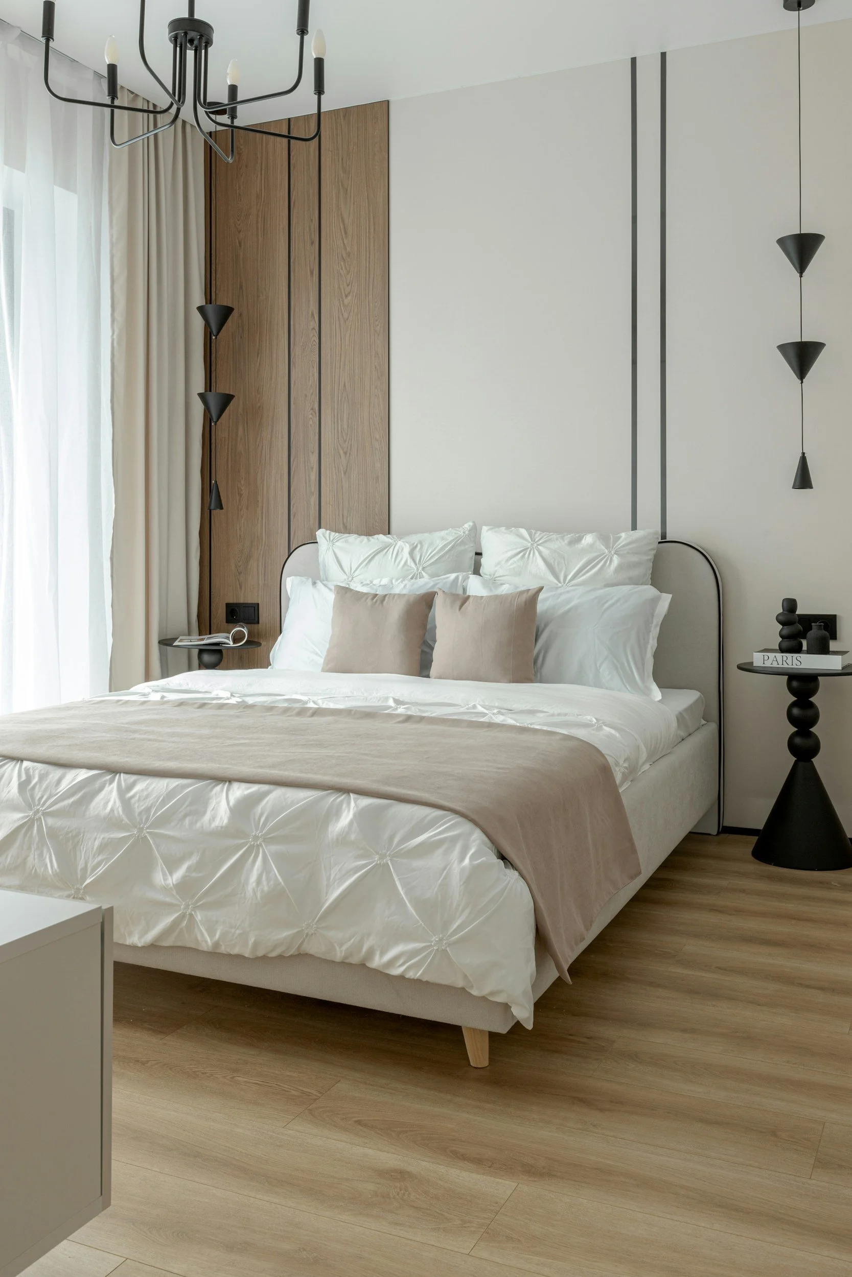 Modernes Schlafzimmer mit weißer Bettwäsche, beige Kissen, dunklen Lampen und einer geometrischen Deckenleuchte.