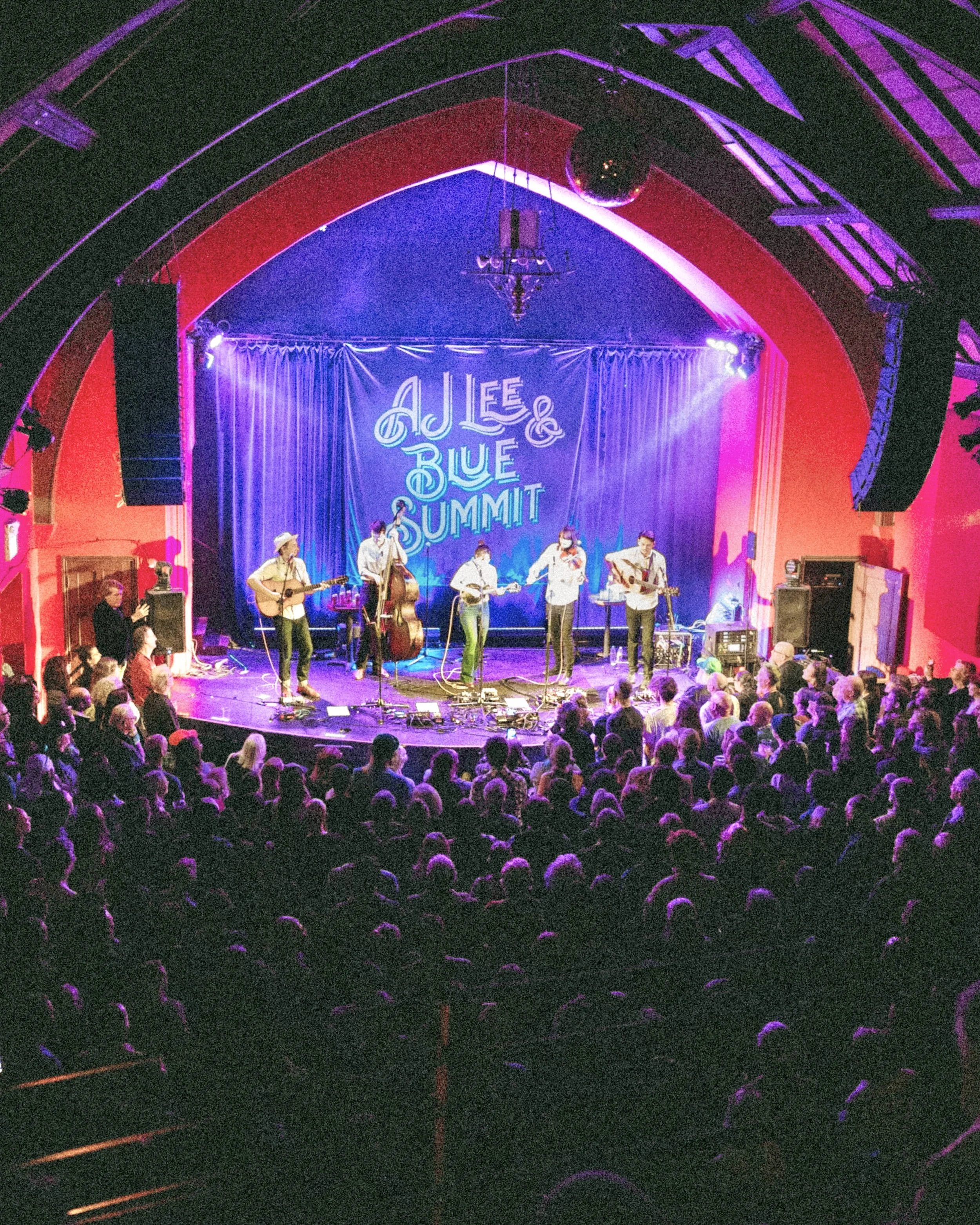 Musicians performing on stage at the AJLE & Blue Summit event, with audience members watching.