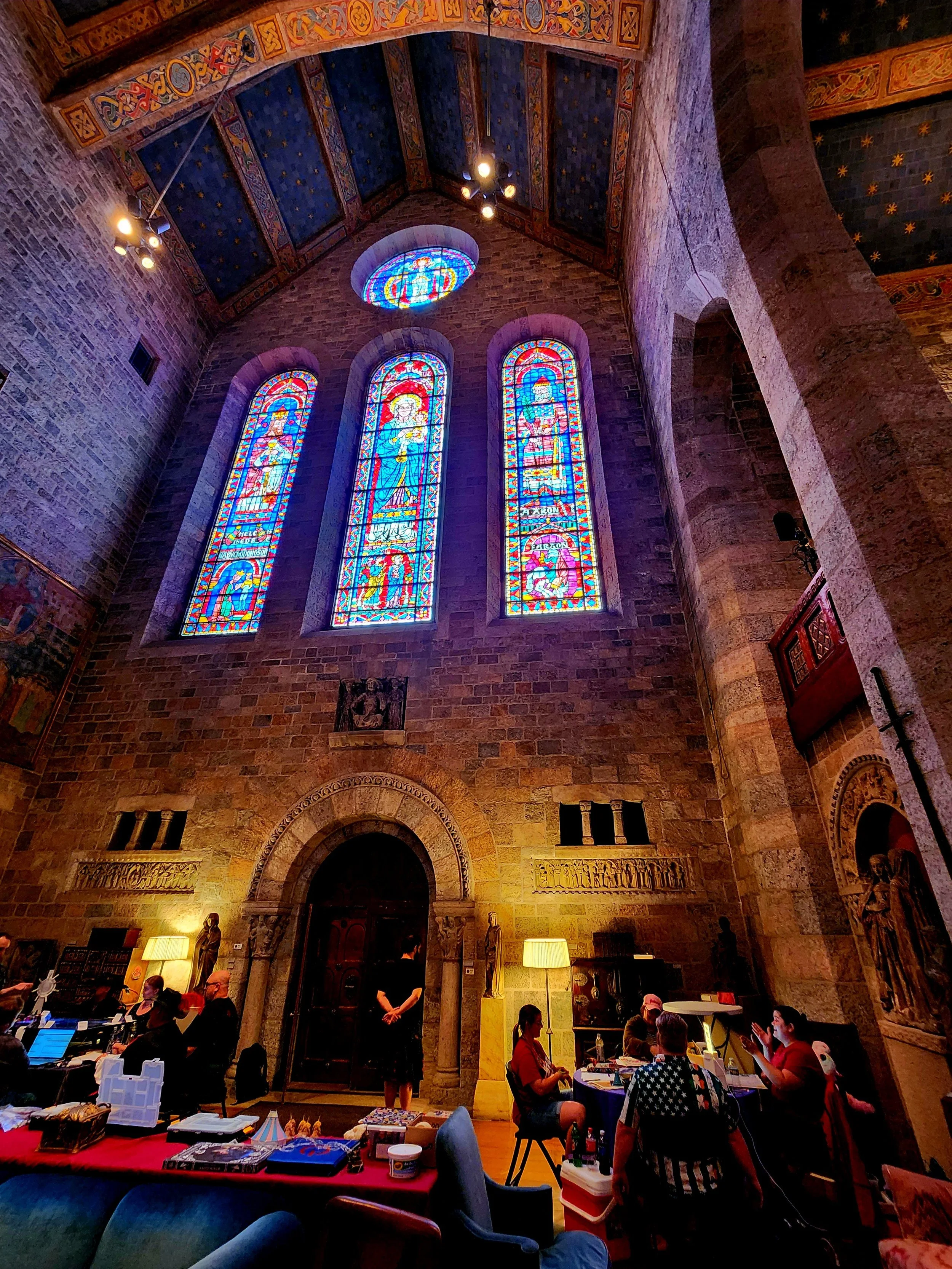 People playing a tabletop RPG game around a table in a castle with stone walls, sculptures, and wooden floors.