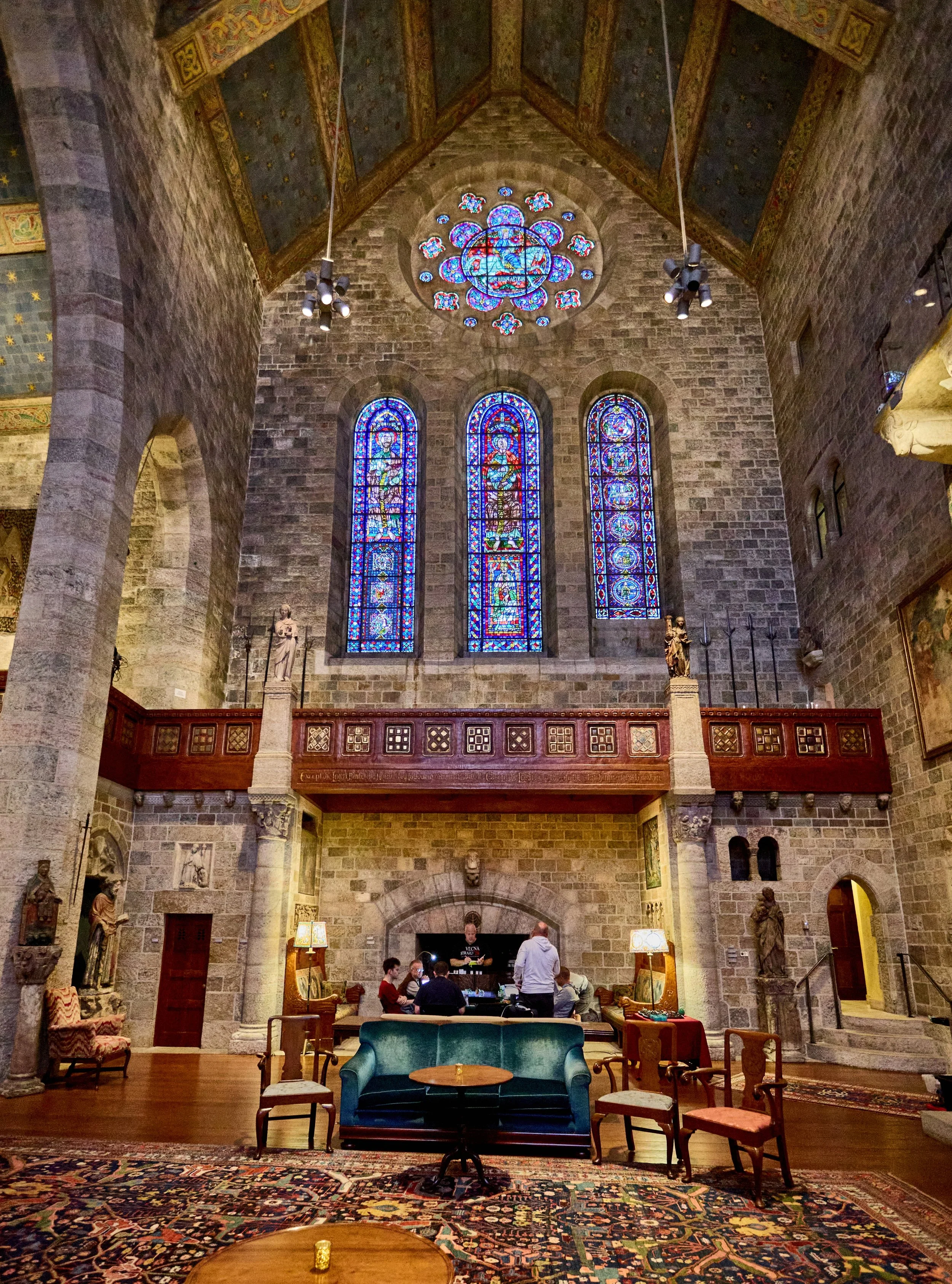 People playing a tabletop RPG game around a table in a castle with stone walls, sculptures, and wooden floors.