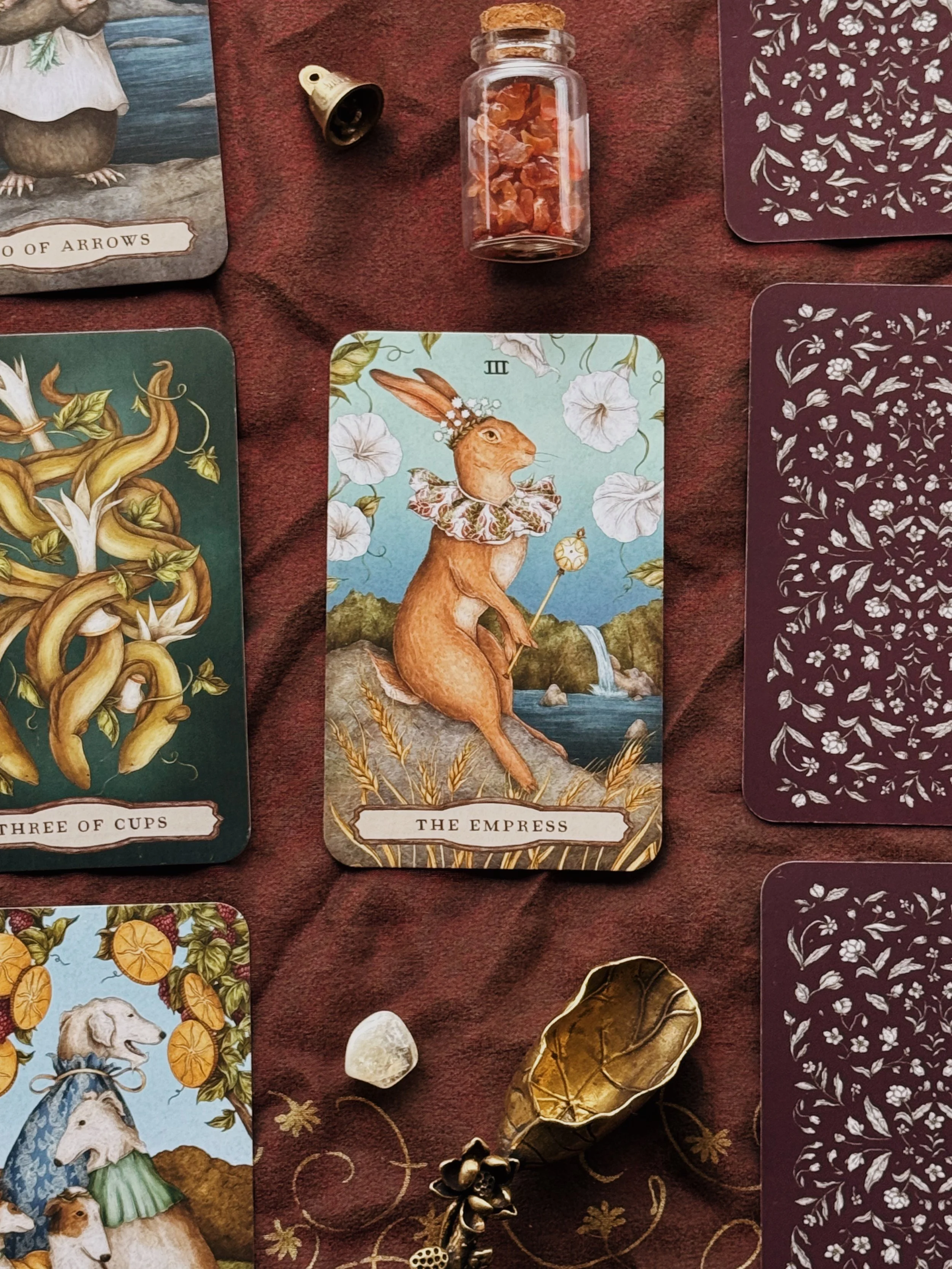 Tarot cards laid out on a dark surface with scattered flower petals, small colorful stones, and tea light candles.