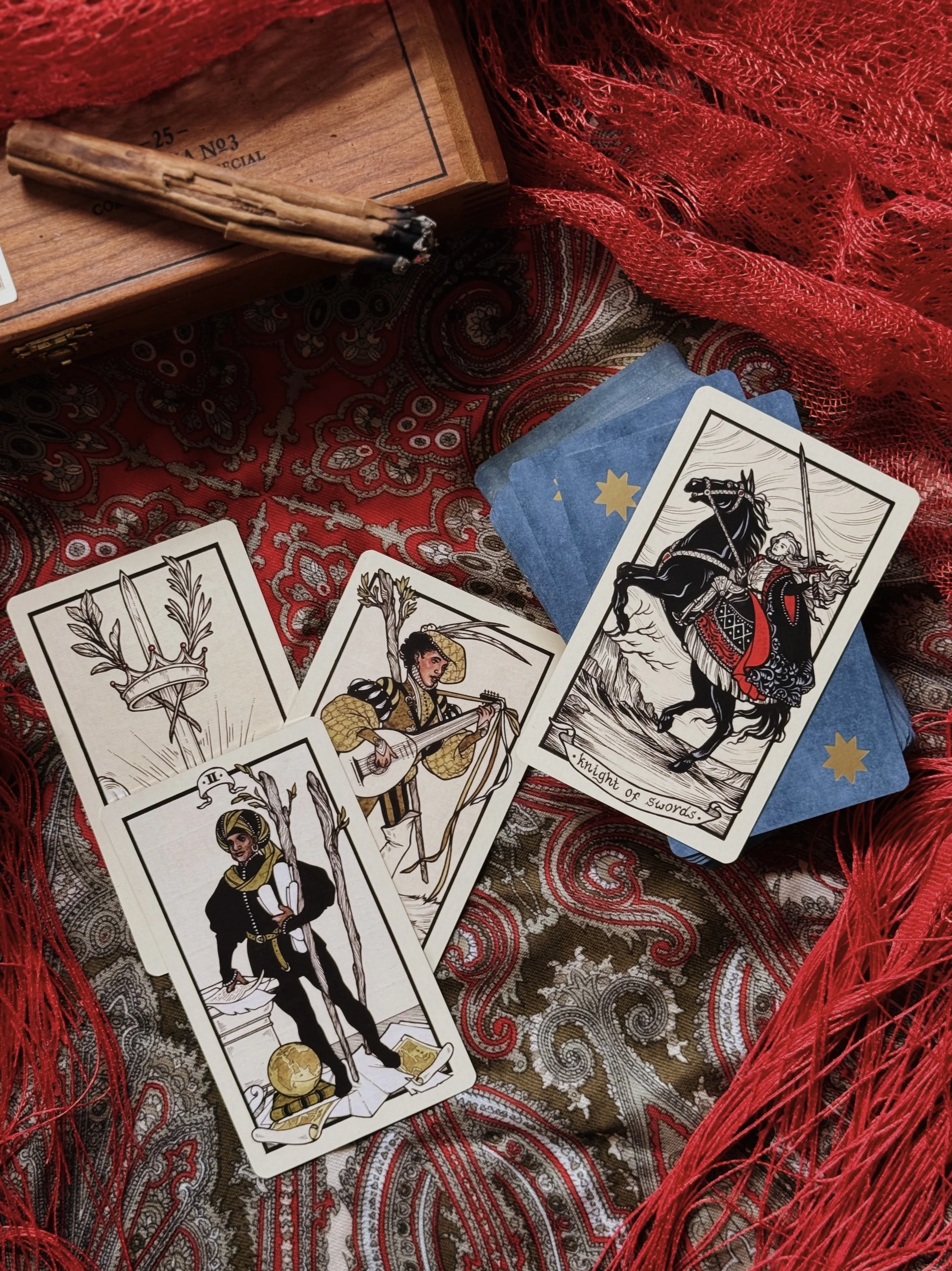A set of tarot cards spread over a black and gold surface, featuring a prominent card depicting a woman dressed in a blue cloak with a bow, holding a scroll, surrounded by symbols of the moon and animals, with other tarot cards partially visible.