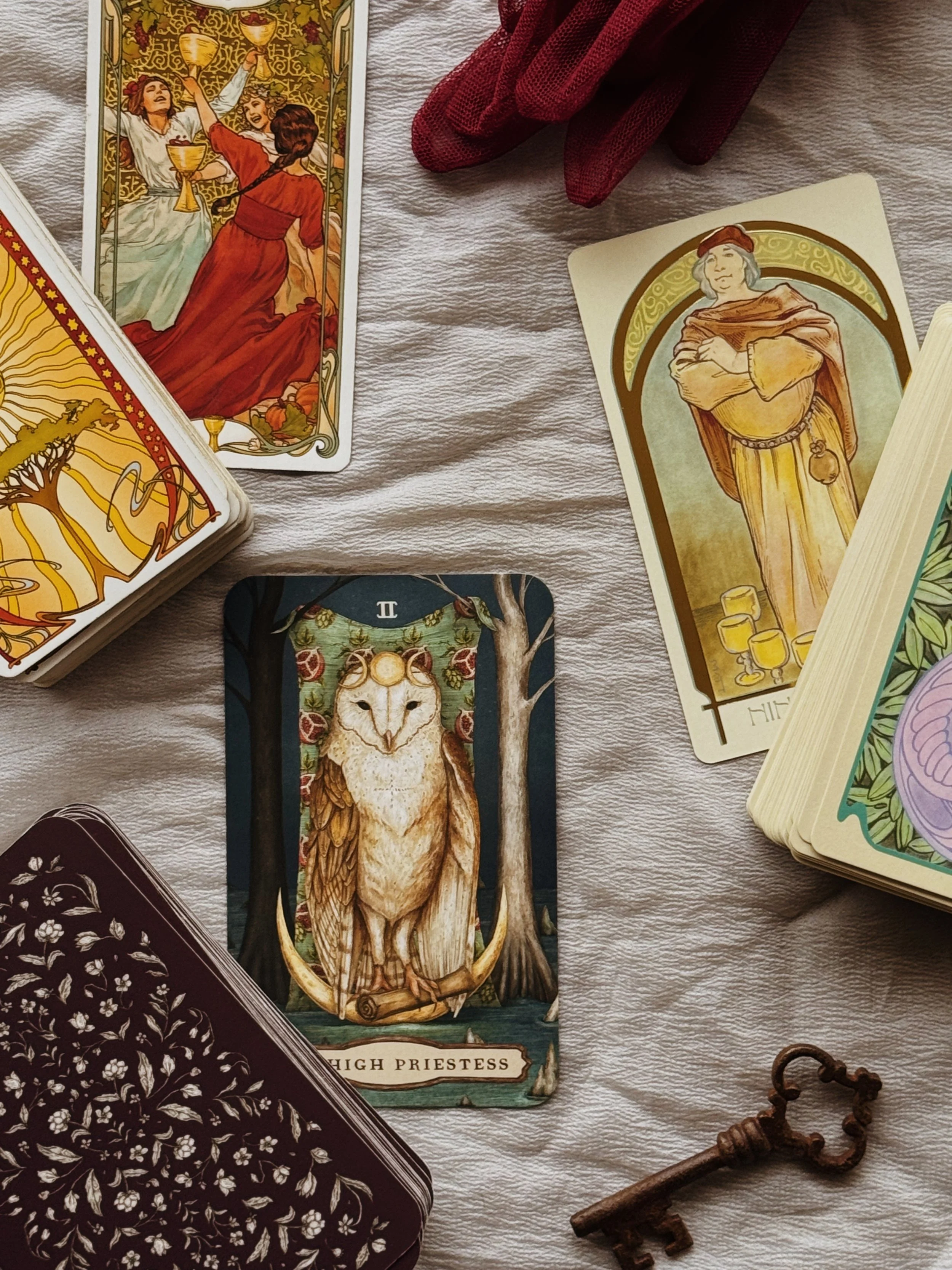 A spread of various tarot  cards depicting celestial symbols, mythological figures, and Victorian-style illustrations, arranged on a fabric surface with decorative stones and a white cloth.