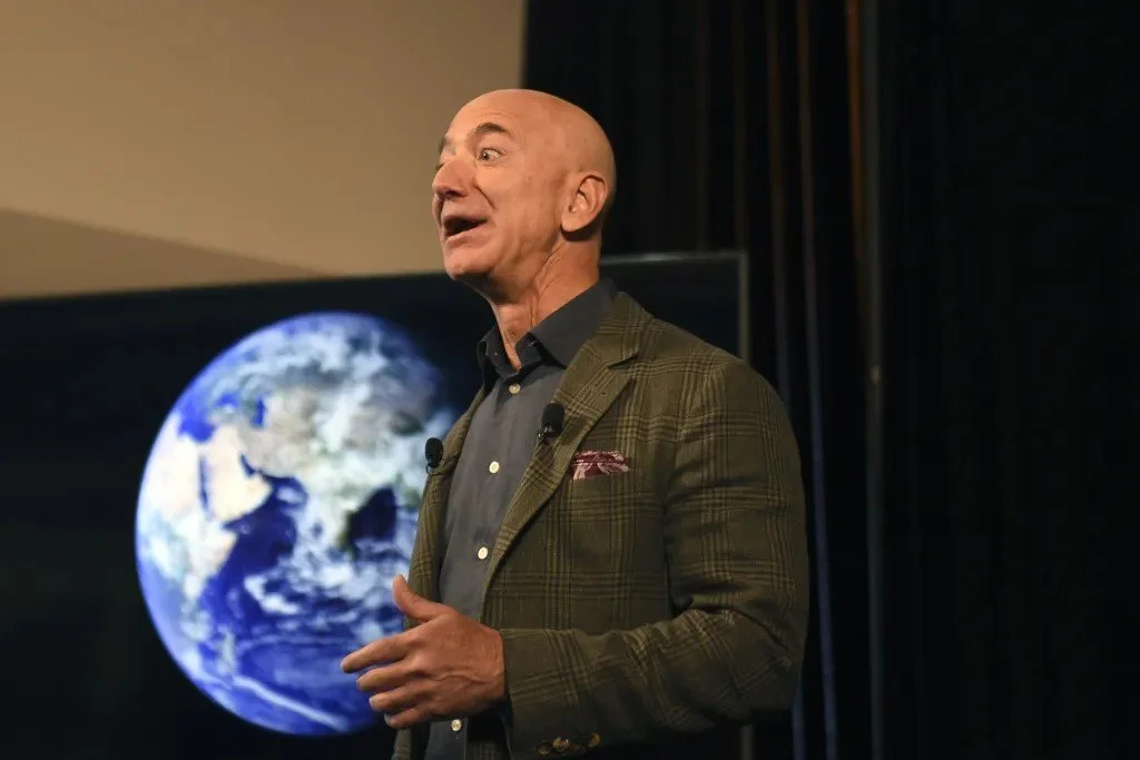 A man in a plaid blazer speaking in front of a large image of Earth projected on a screen.