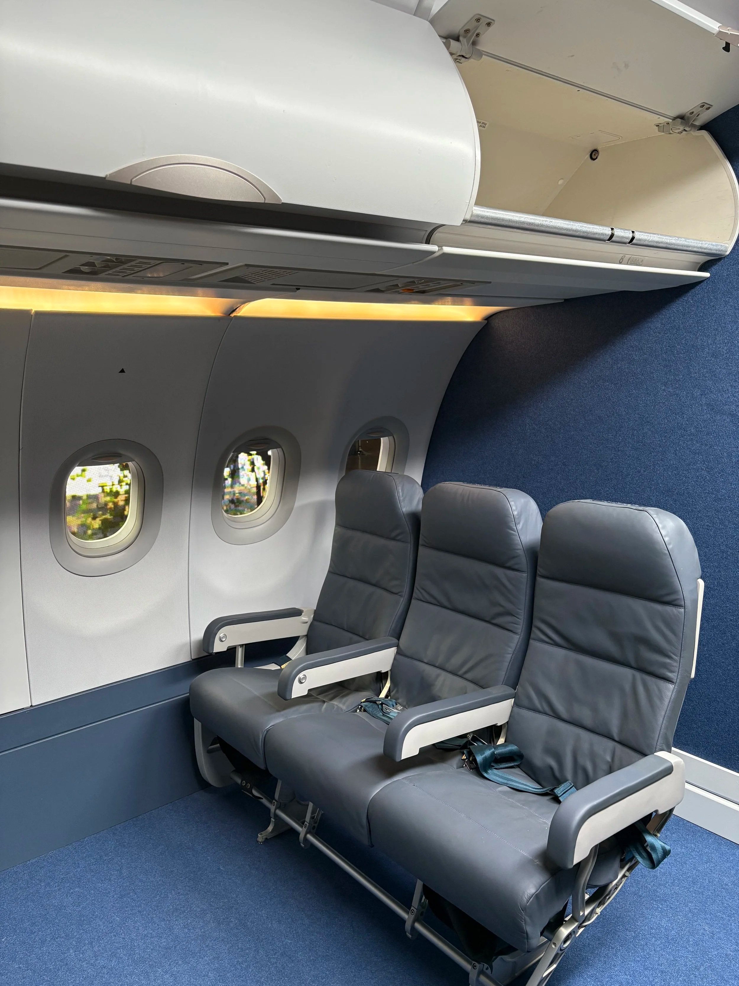 Empty airplane seats next to a window, with blue carpet and a white wall.