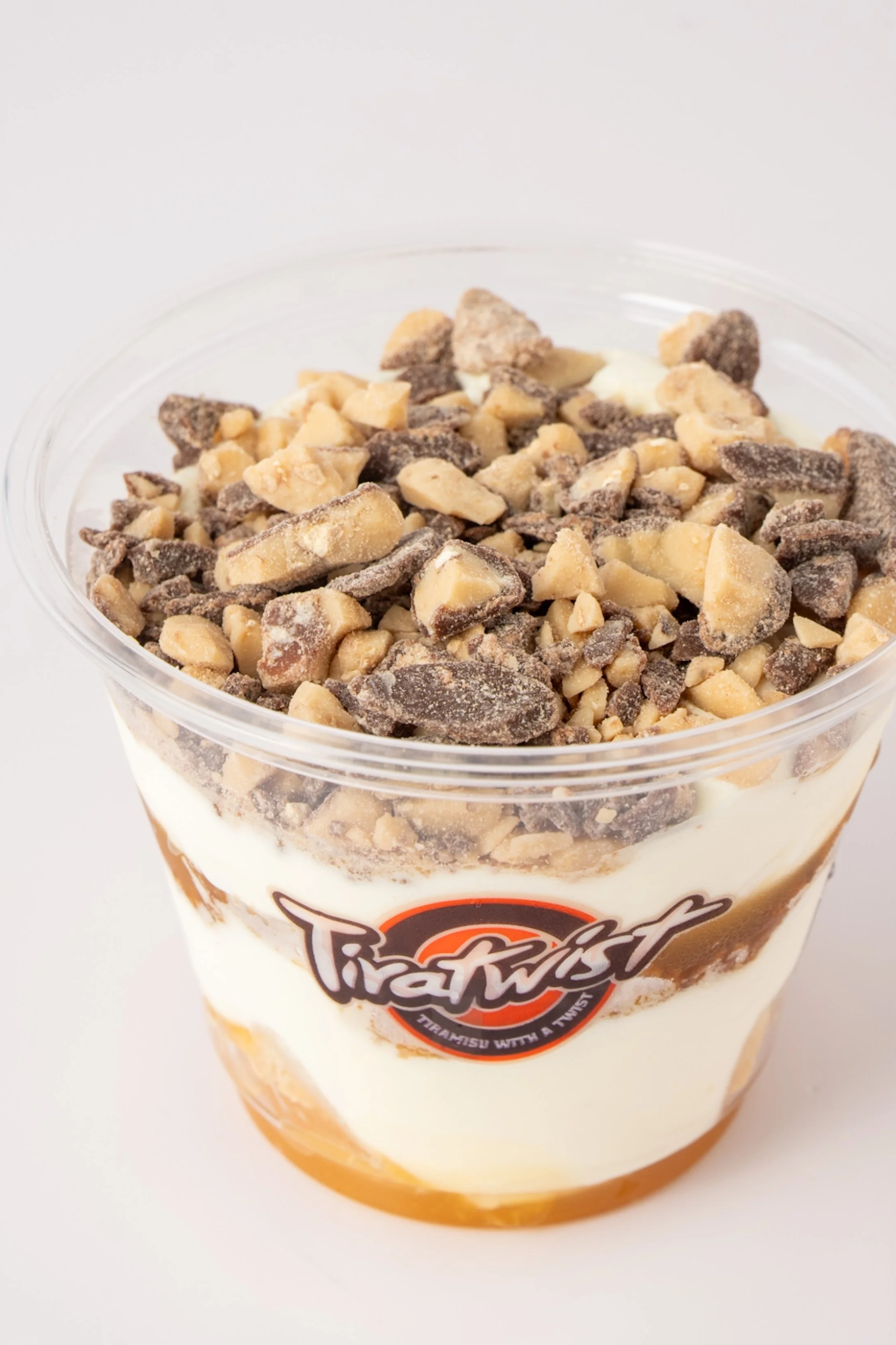 A cup of tiramisu with crushed toffee on top and a logo that says Tiratwist.