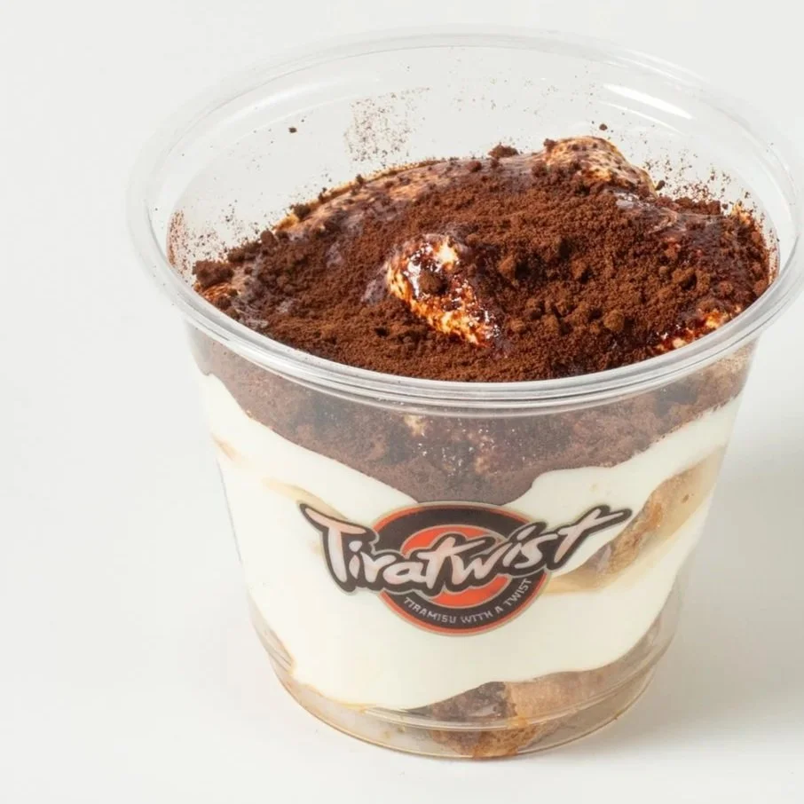 A clear plastic cup with tiramisu topped with cocoa powder and a logo that reads 'TiraTwist' with the tagline 'Tiramisu with a twist'.