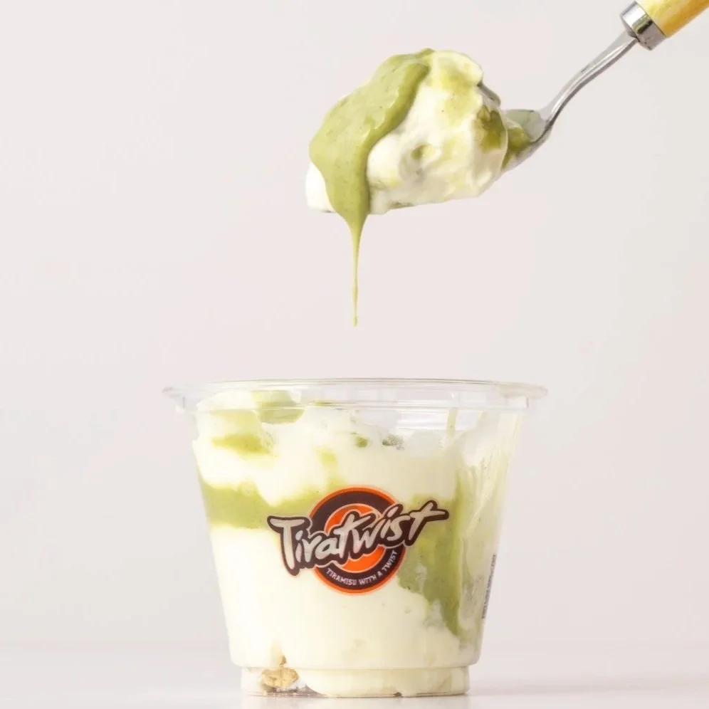 A spoon with green and white ice cream being lifted above a clear plastic cup filled with similar mascarpone, with a brand logo that reads 'TiraTwist' on the cup.