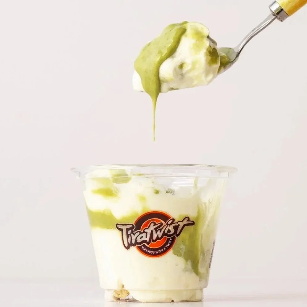 A spoon with green pistachio and white soft mascarpone above a plastic cup with matching green and white swirls, labeled "TiraTwist."