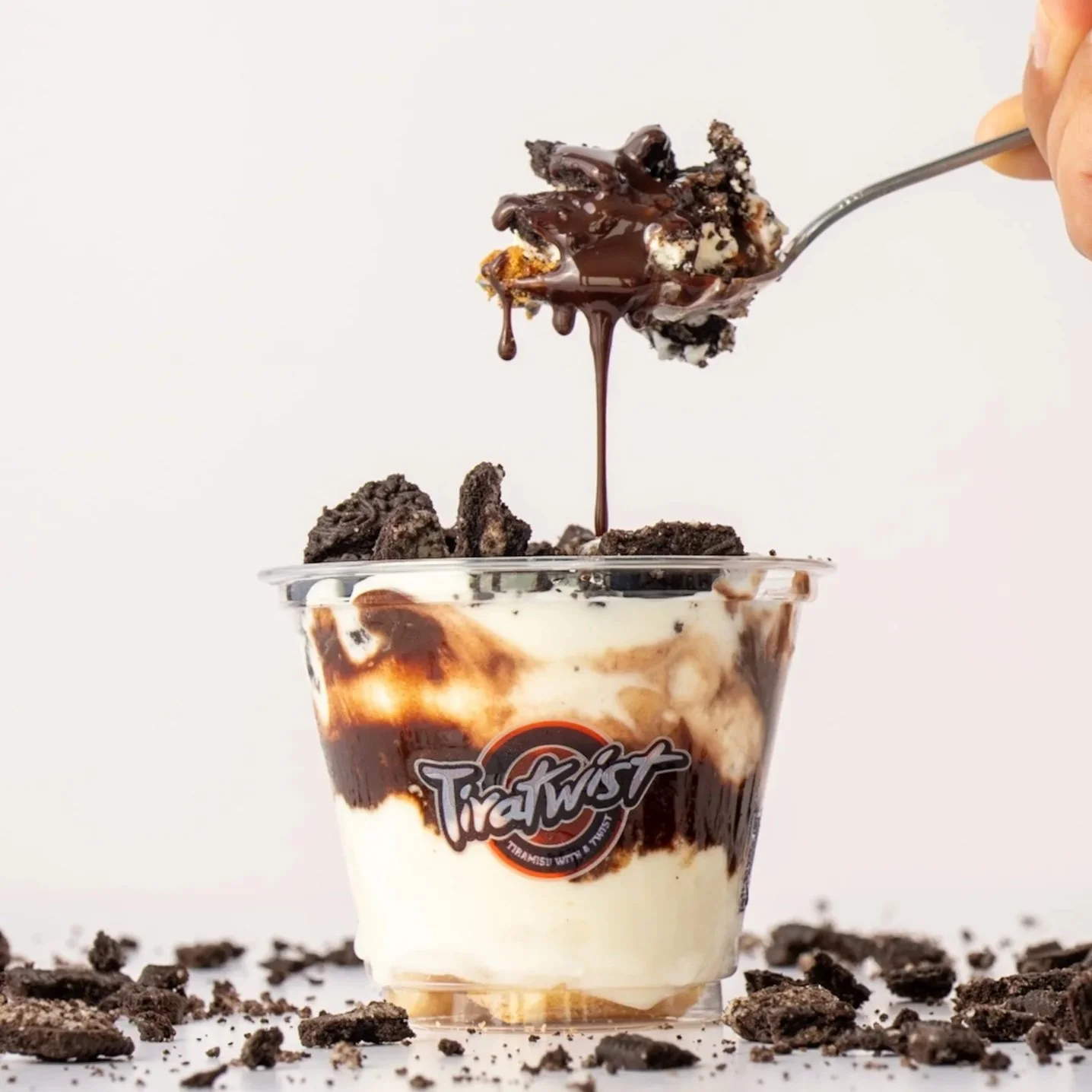 Close-up of a layered dessert in a glass jar with whipped cream, chocolate pieces, and a biscuit layer.