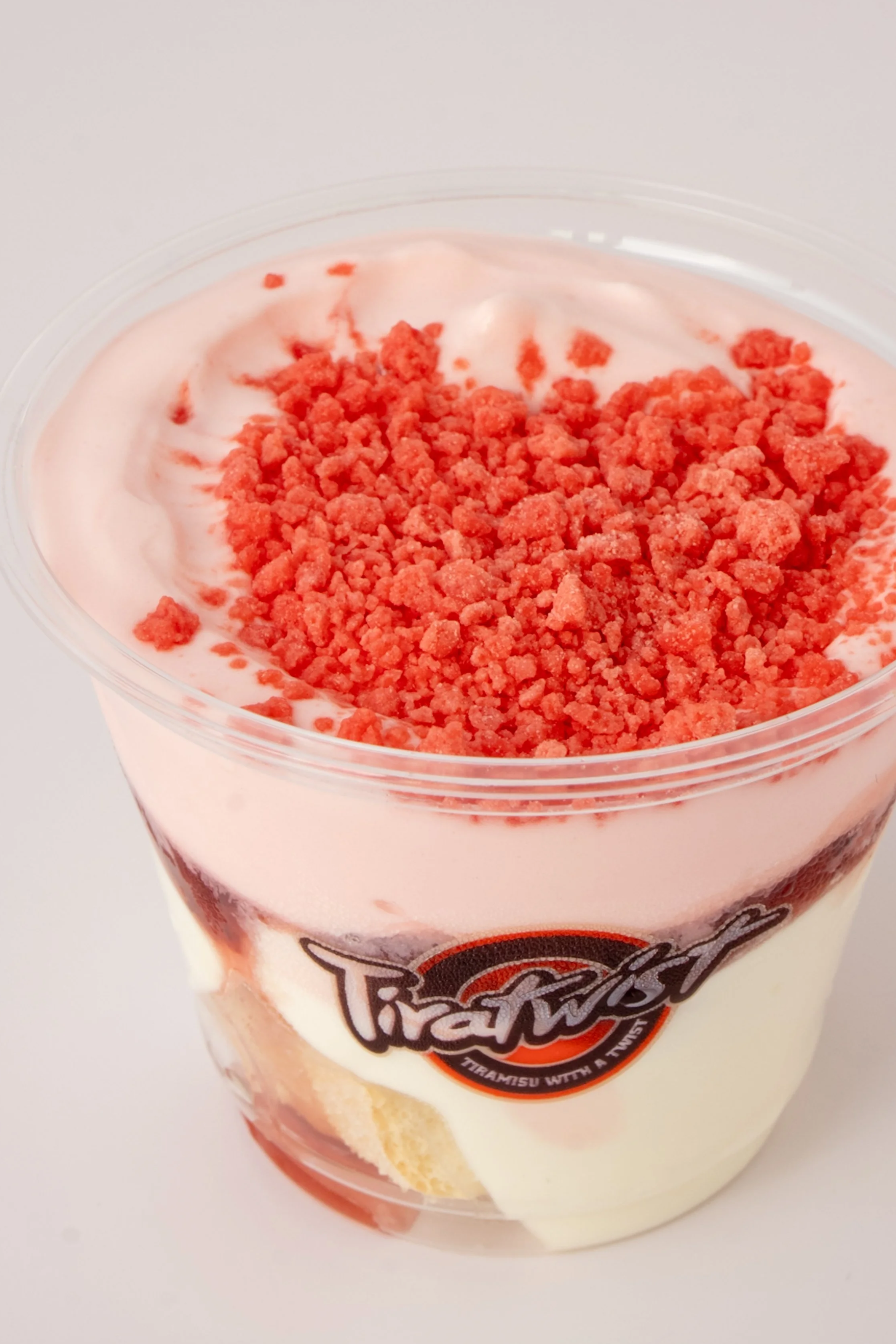 A cup of strawberry shortcake-flavored Tiramisu dessert with layers of cream, strawberries, and crumbles on top.
