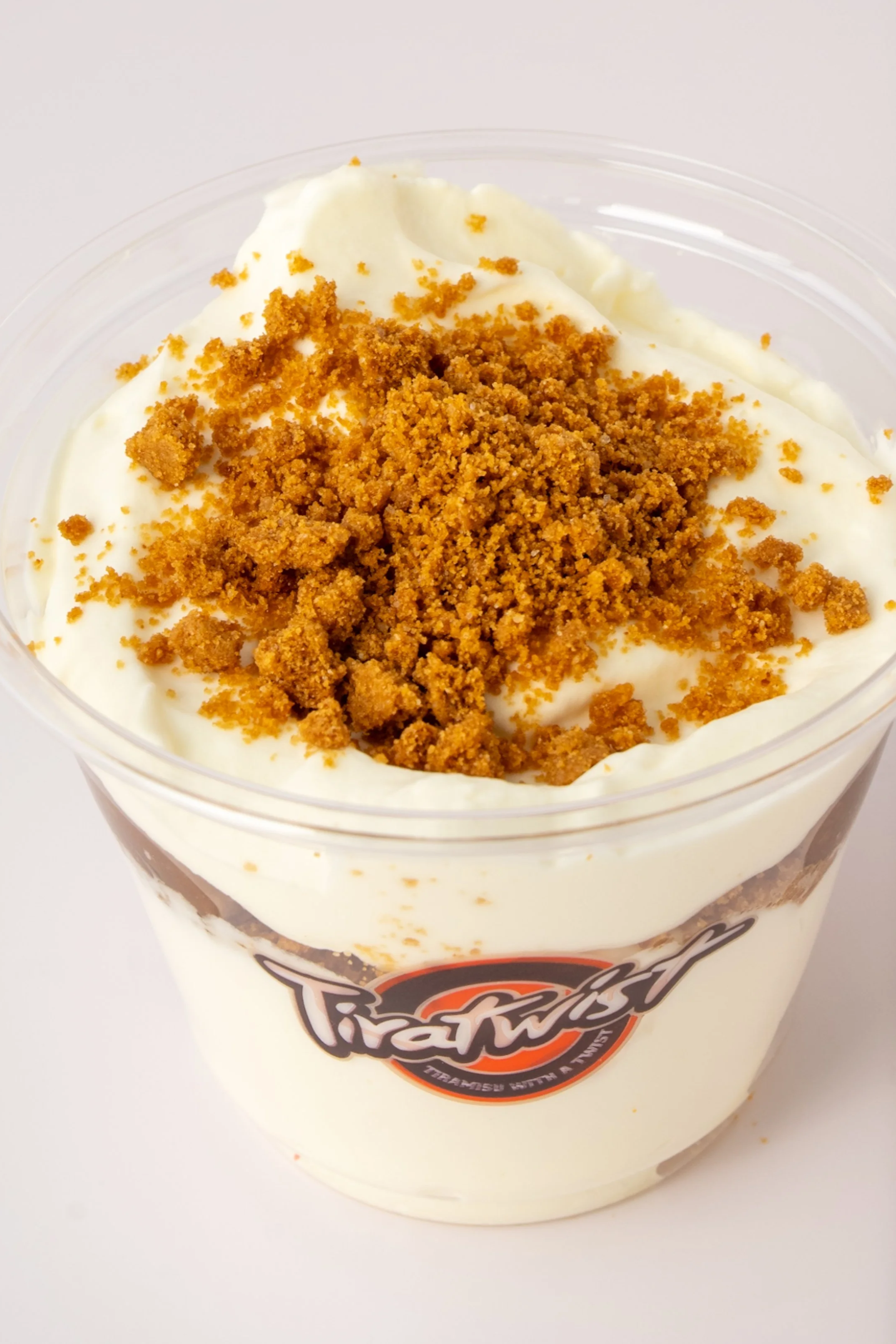 A clear plastic cup filled with mascarpone topped with crushed graham crackers.