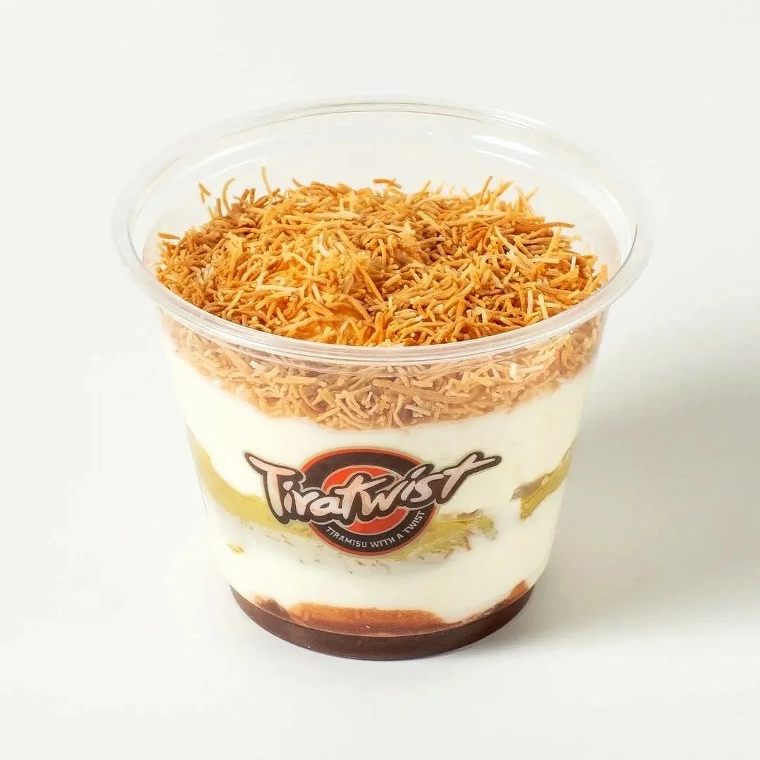 A clear plastic cup with layered ingredients, including shredded toasted kataifi on top, labeled 'Tiratwist'.