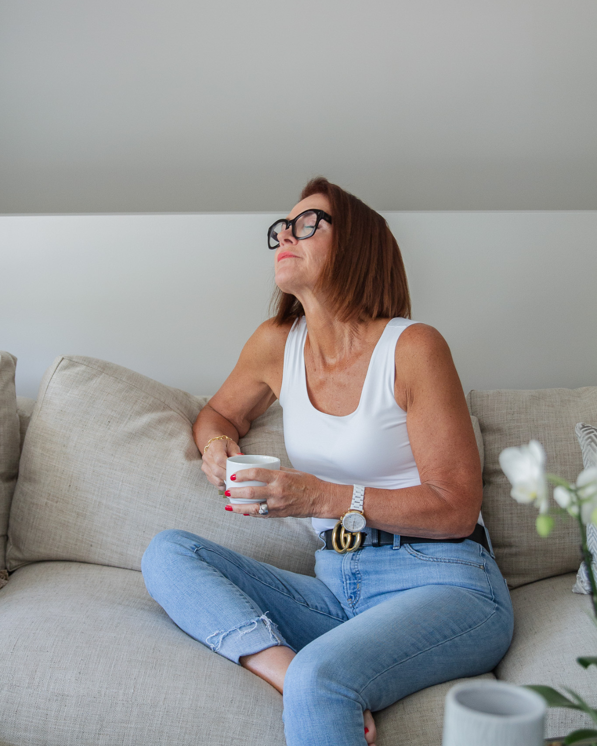 Woman sitting on a couch holding a cup of coffee, reflecting quietly, representing trust, faith, and mindful wellness