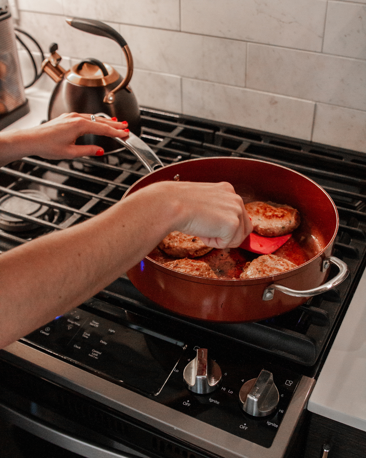 Caroline flipping ground turkey burgers in a terracotta colored pan on the stove.