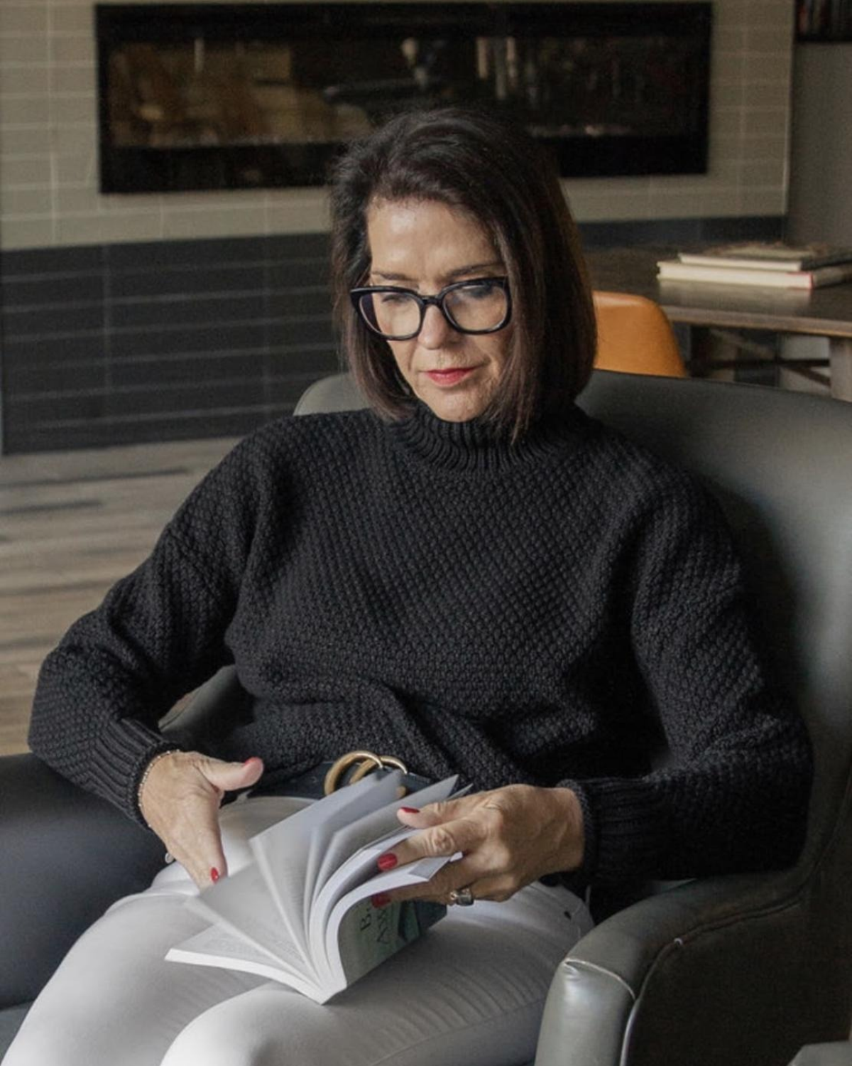 Kelly of @Well sitting in a chair and reading a book.