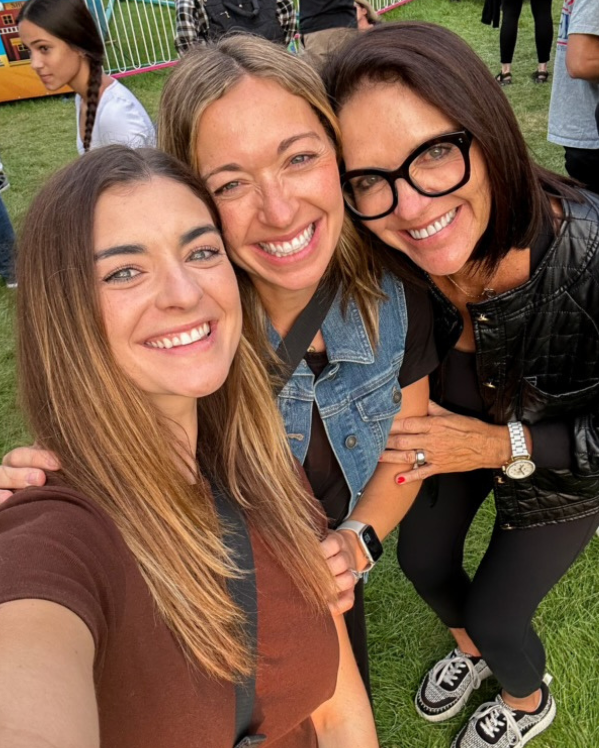 Three women smiling together at an outdoor event, illustrating the importance of connection, belonging, and mother-daughter relationships across generations.