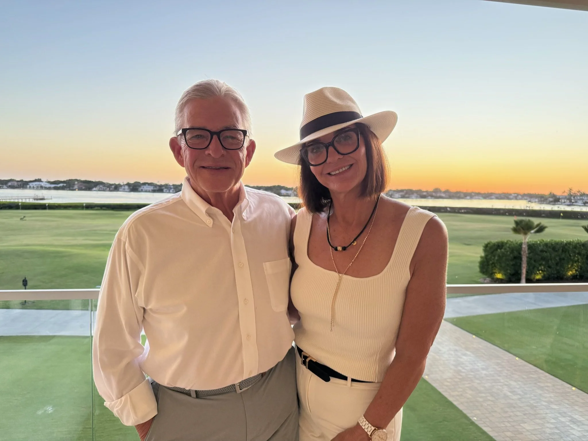 Kelly and her husband smile together outdoors at sunset overlooking the water.