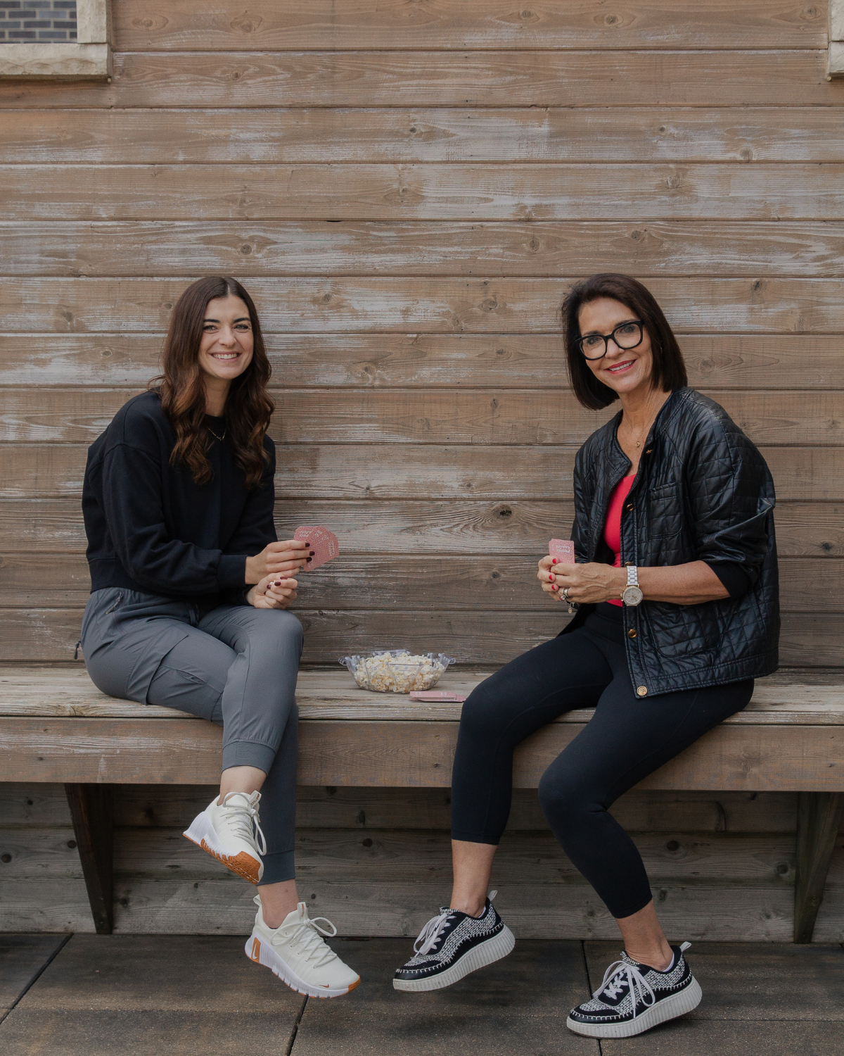 Kelly and Caroline sit outdoors playing cards together, representing balance, connection, and enjoying summer while maintaining healthy habits.