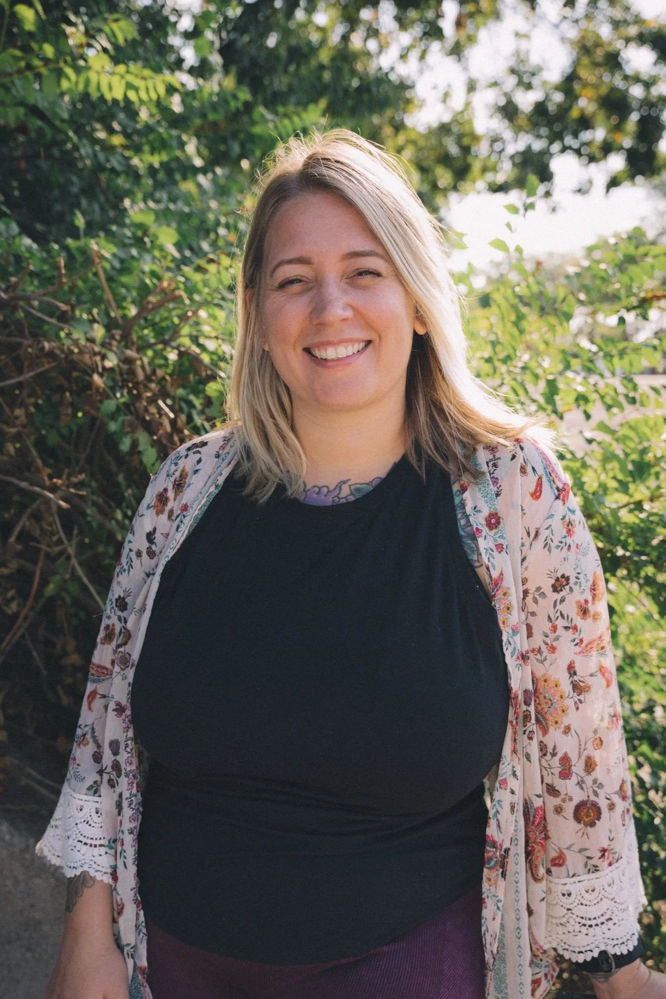A woman smiling outdoors with a floral cardigan.