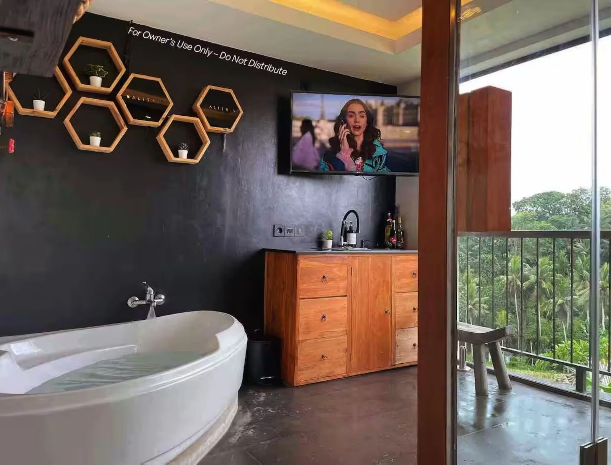 Bathroom with bathtub, wooden cabinet, TV on black wall, and balcony with green view