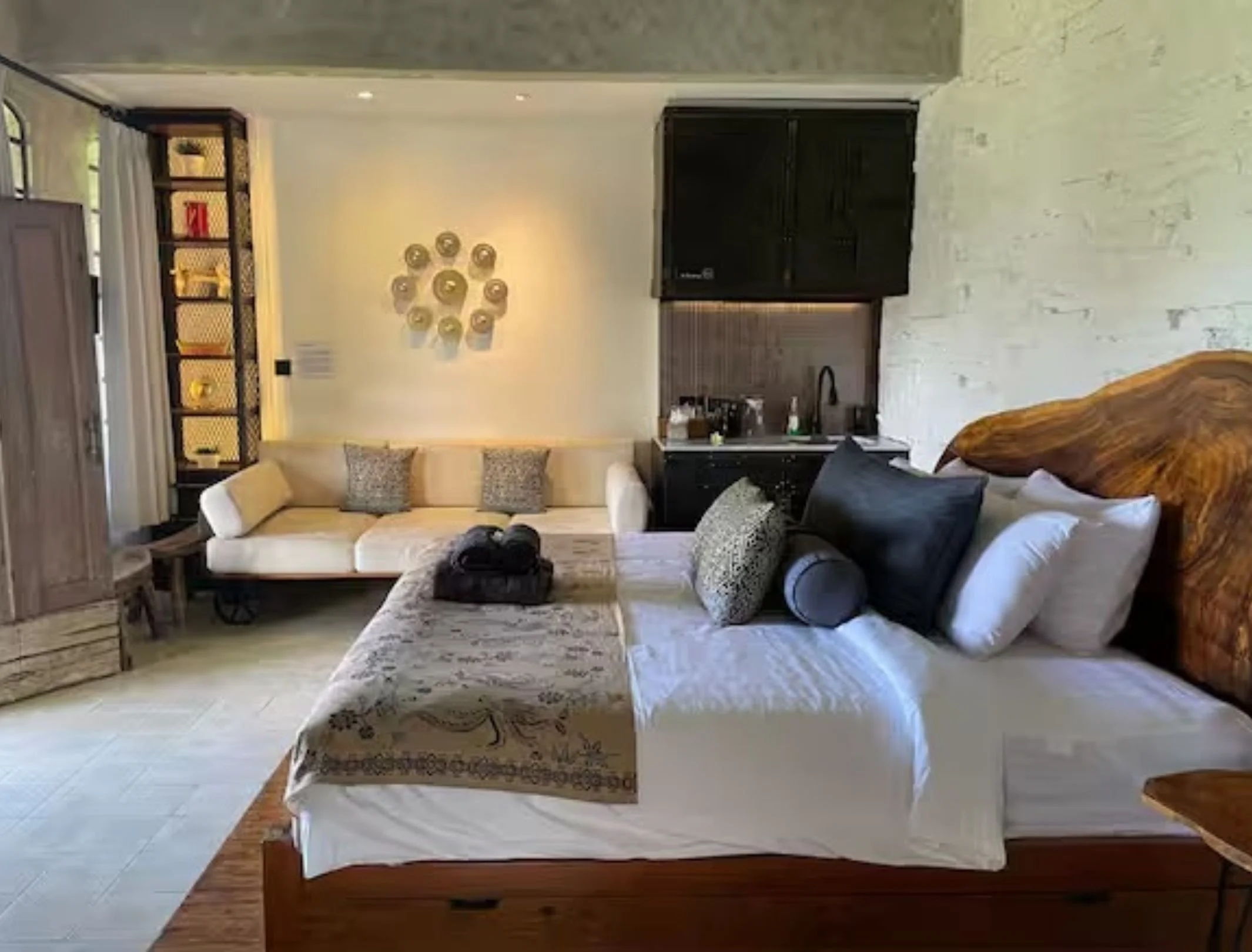 Interior of a cozy living space with a bed, sofa, and kitchenette, decorated with neutral tones and modern design elements.
