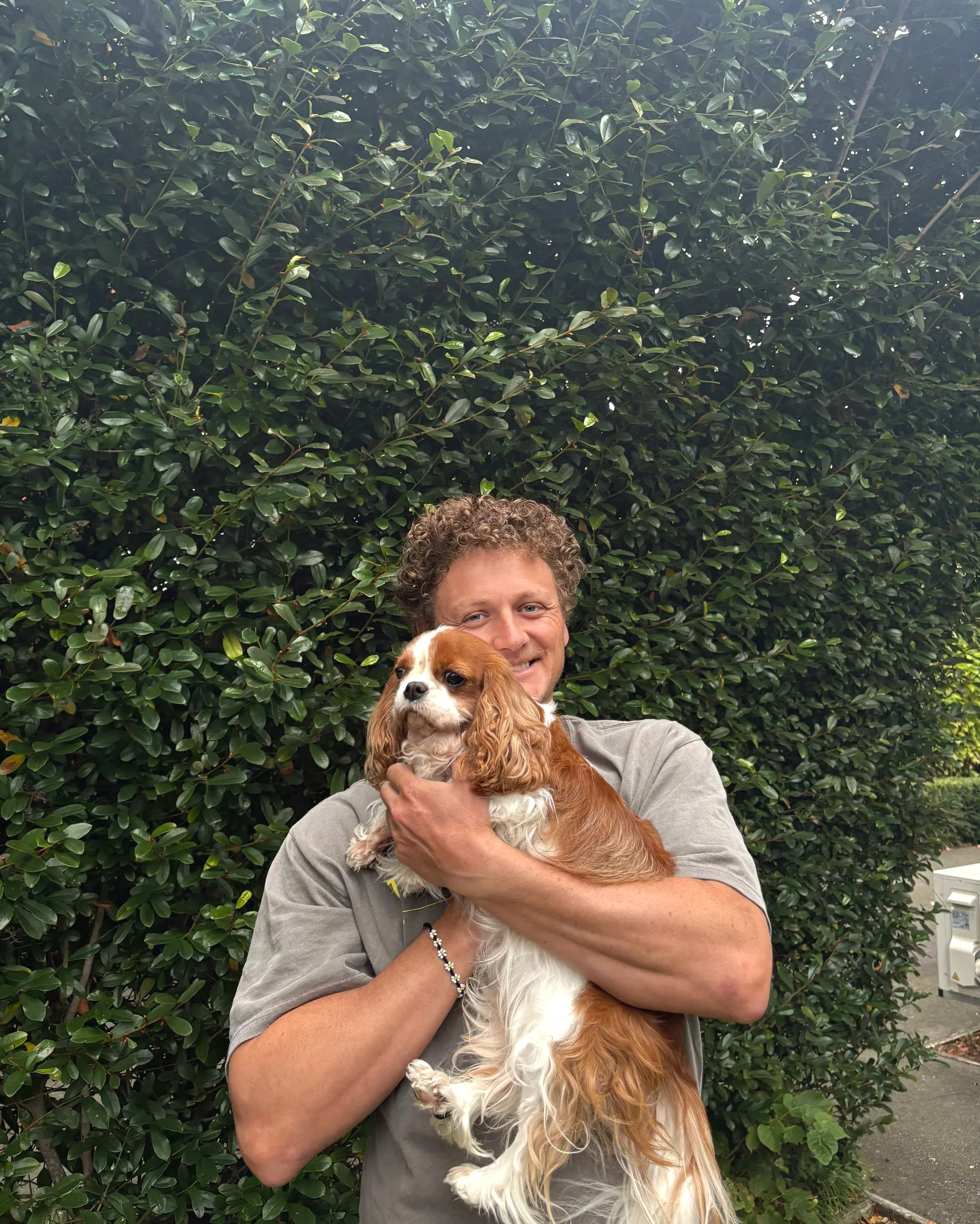 Lachie holding a dog in front of a green hedge.
