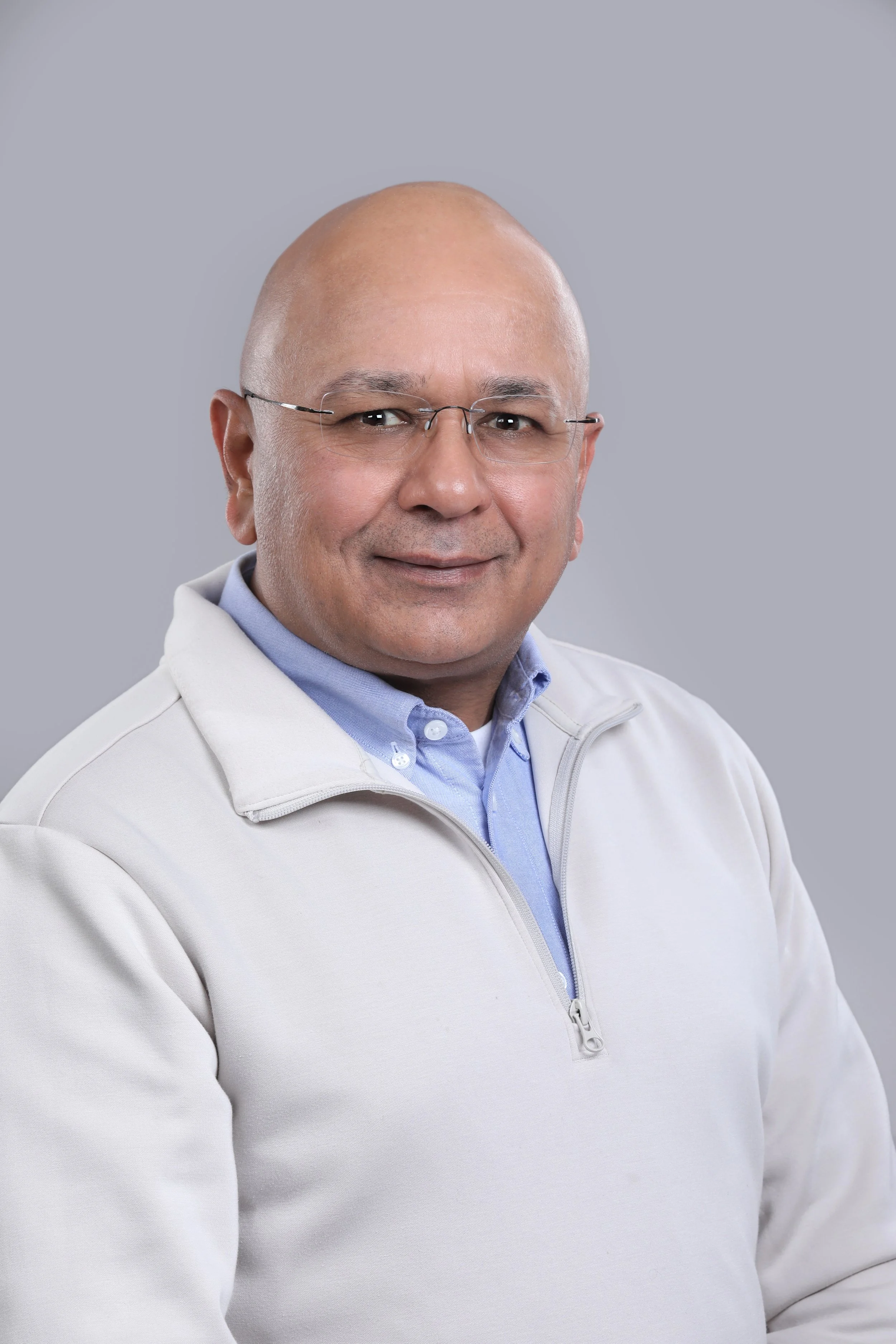 A middle-aged man with glasses and a bald head, wearing a light-colored jacket and a blue collared shirt, smiling.