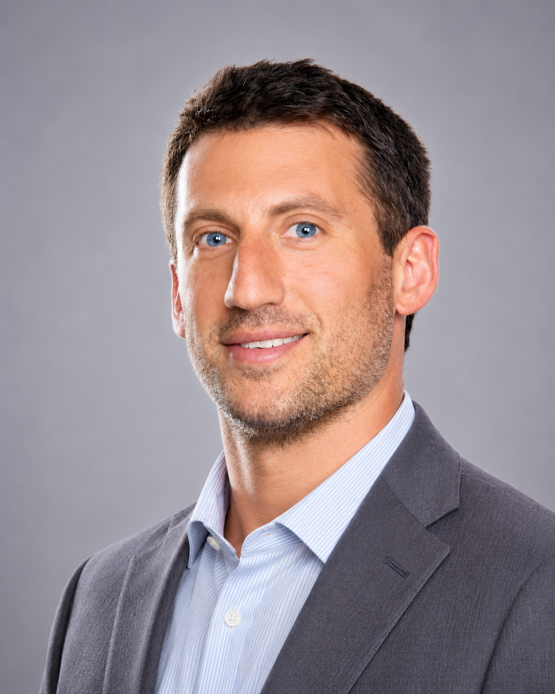 A professional headshot of a man in a suit with a gray background.