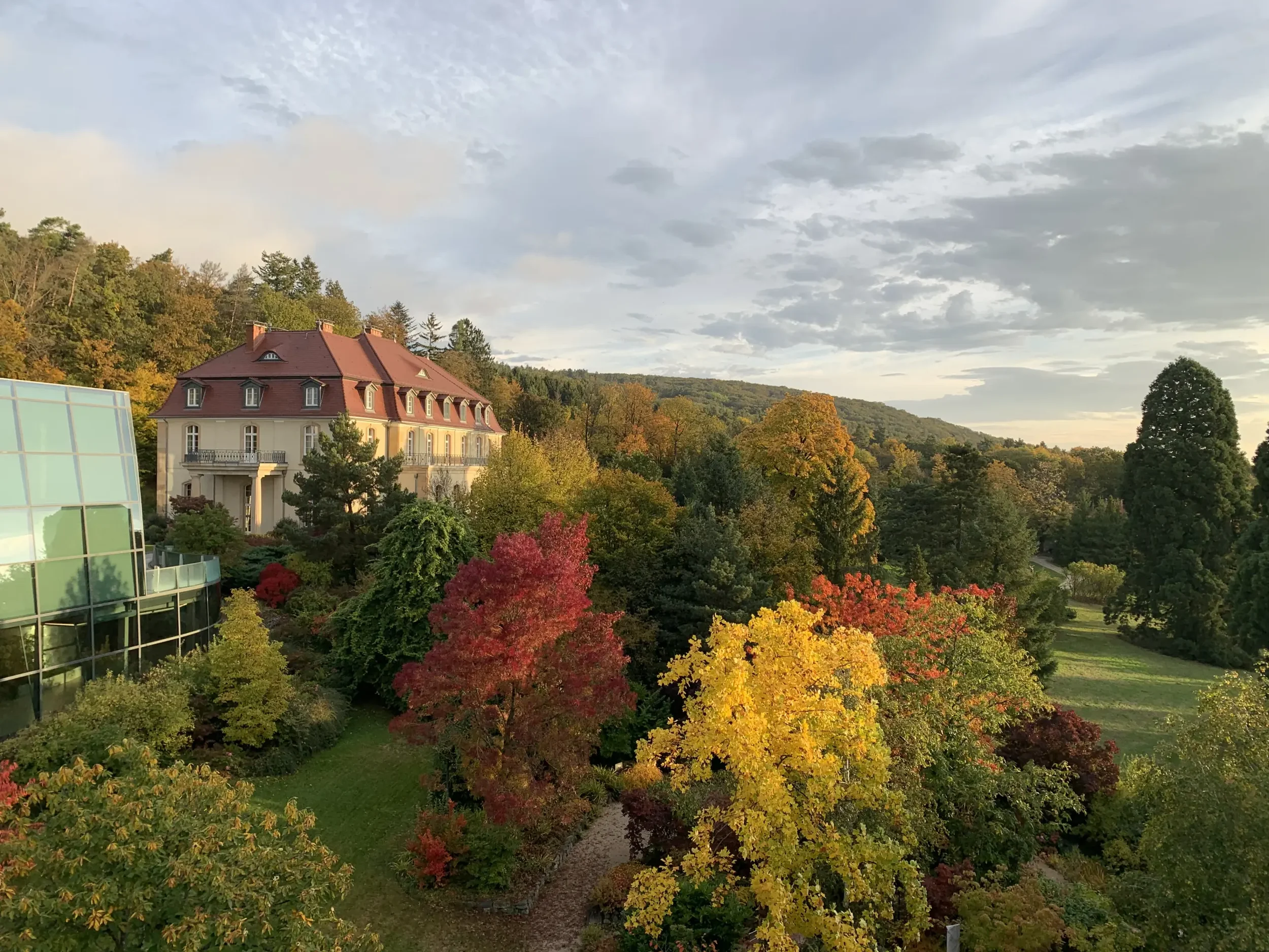 Ein großes Haus mit rotem Dach inmitten eines herbstlichen Gartens mit bunten Blättern in rot, gelb und orange.
