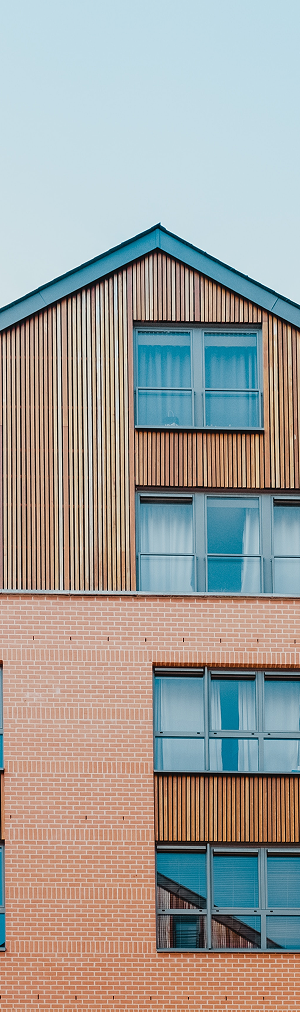 Secteur immobilier : Vue partielle d'un bâtiment avec façade en bois et briques, fenêtres en verre, sous un ciel clair.