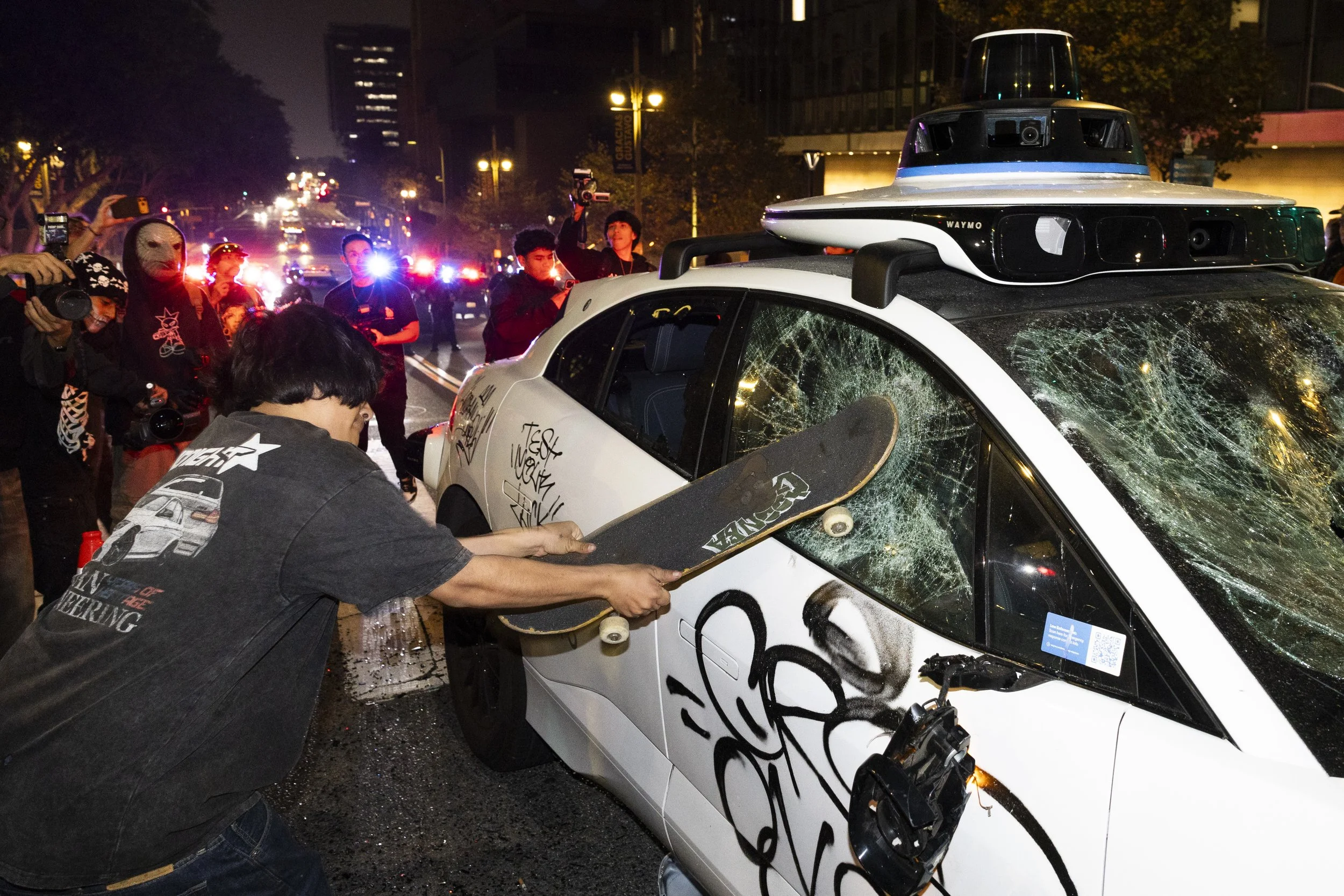 A skateboarder slams his skateboard into a Waymo vehicle line during the Halloween Hellbomb event hosted by Thrasher, Vans, and Monster Energy on Saturday, Oct. 25, 2025, in downtown Los Angeles. The event was declared an unlawful assembly after part