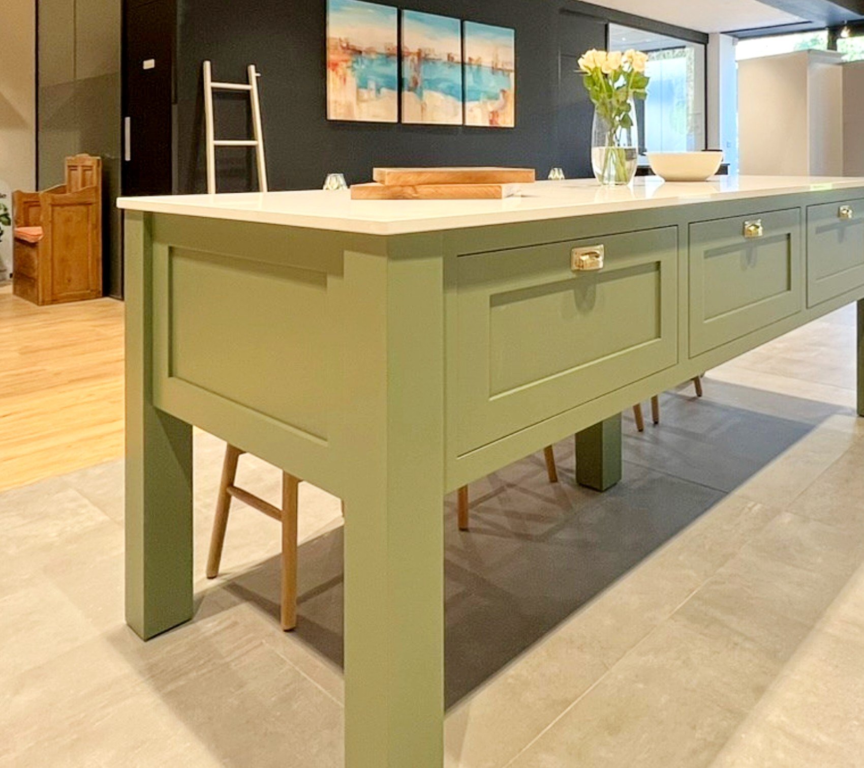 Modern kitchen with green island, light countertops, and bar stools. Decor includes a vase with flowers and abstract artwork on walls.