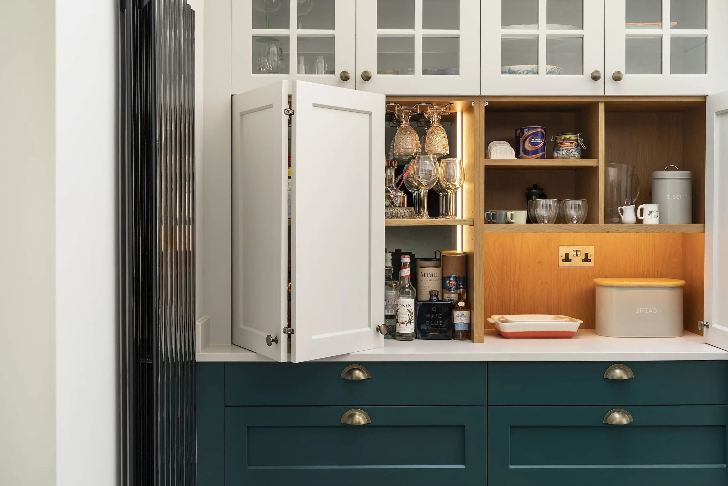 Open cabinet with glassware and lighting, featuring green and white cabinetry below