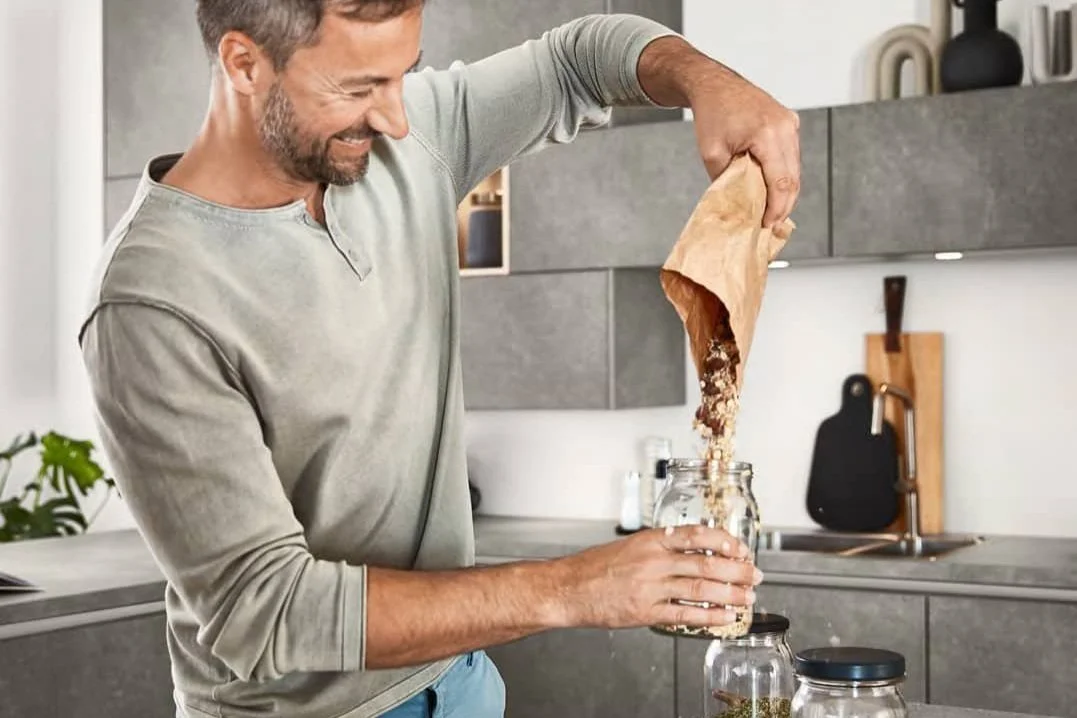 Smiling man filling a jar with dried goods in a contemporary gray kitchen