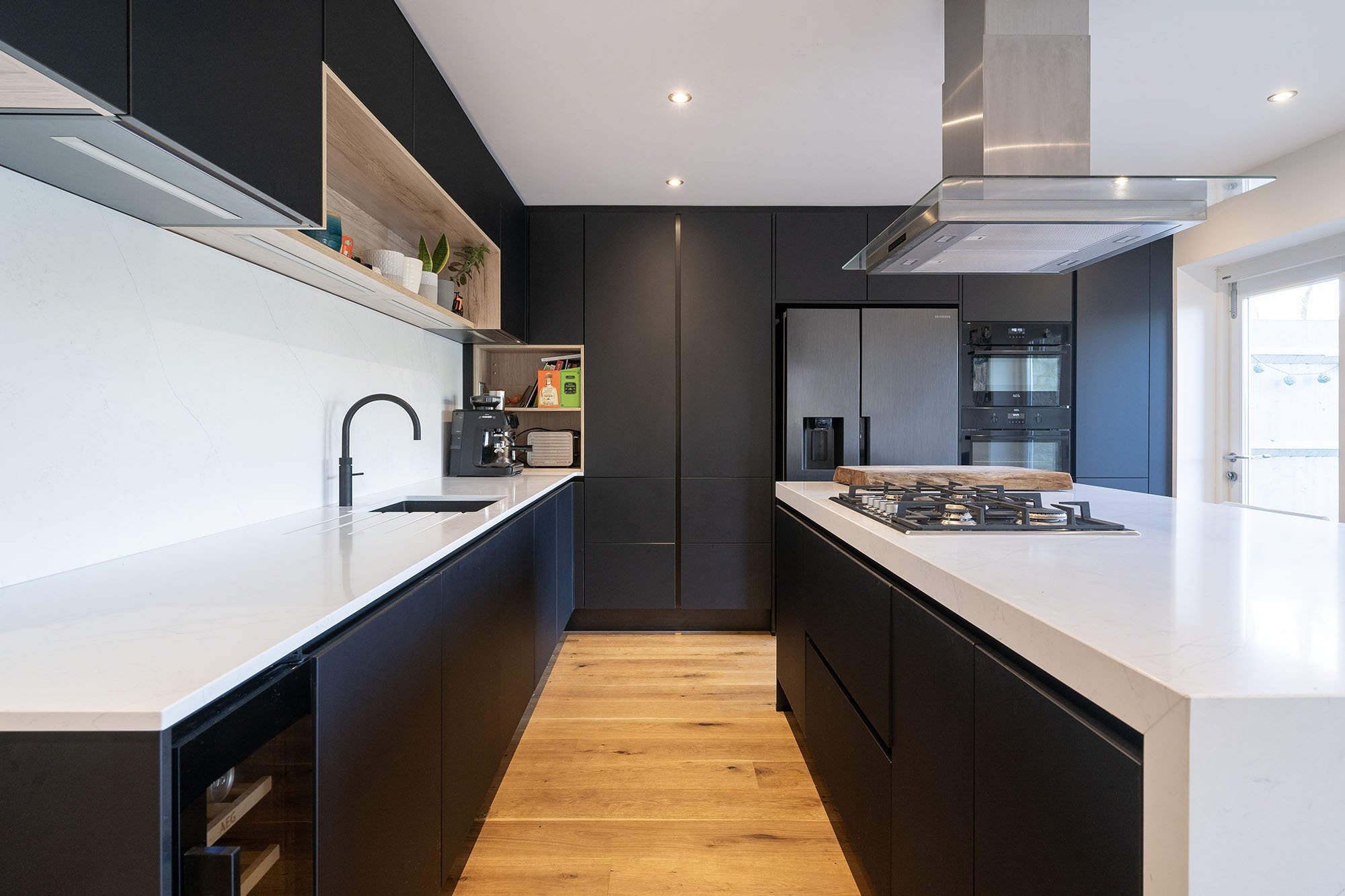 Modern black kitchen with white worktops, open shelving, and wood flooring