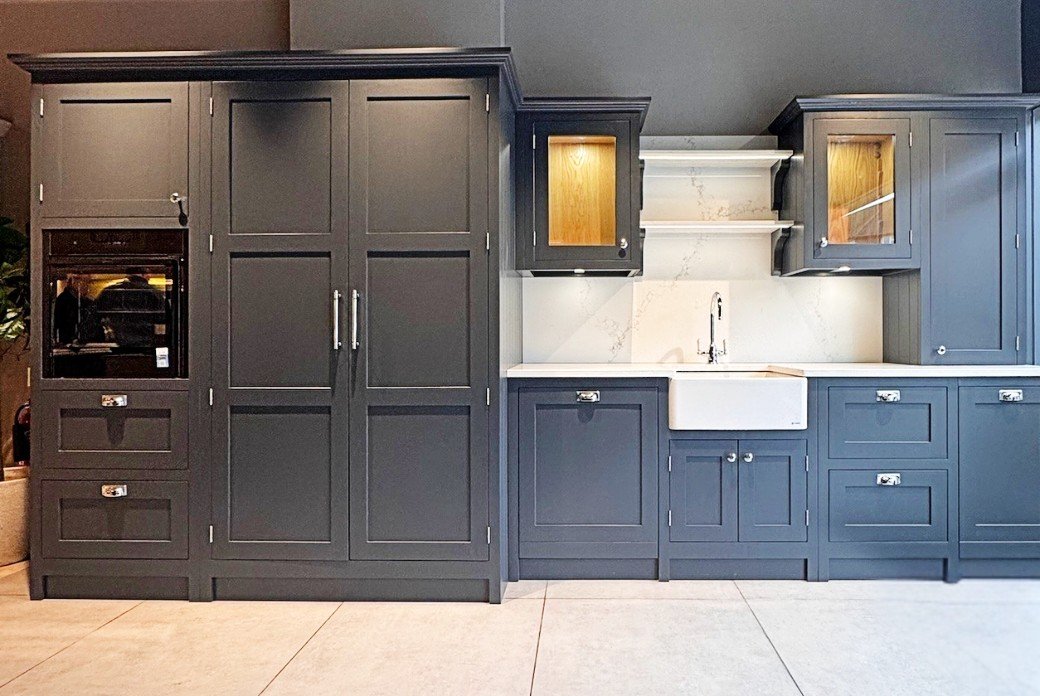 Modern kitchen with gray cabinets, a double-door pantry, built-in oven, and farmhouse sink. Features marble backsplash and open shelves.