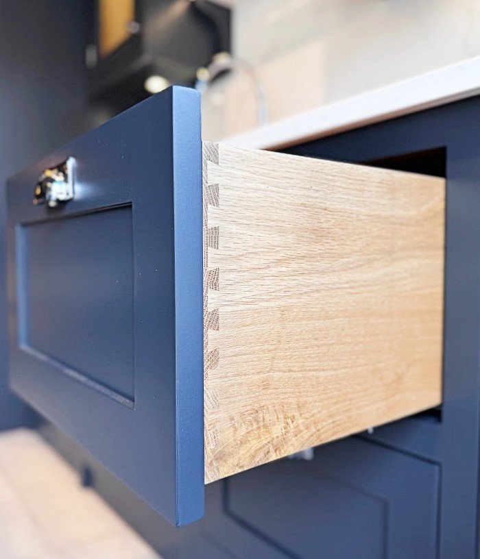 Open wooden drawer with dovetail joints in a navy blue cabinet.