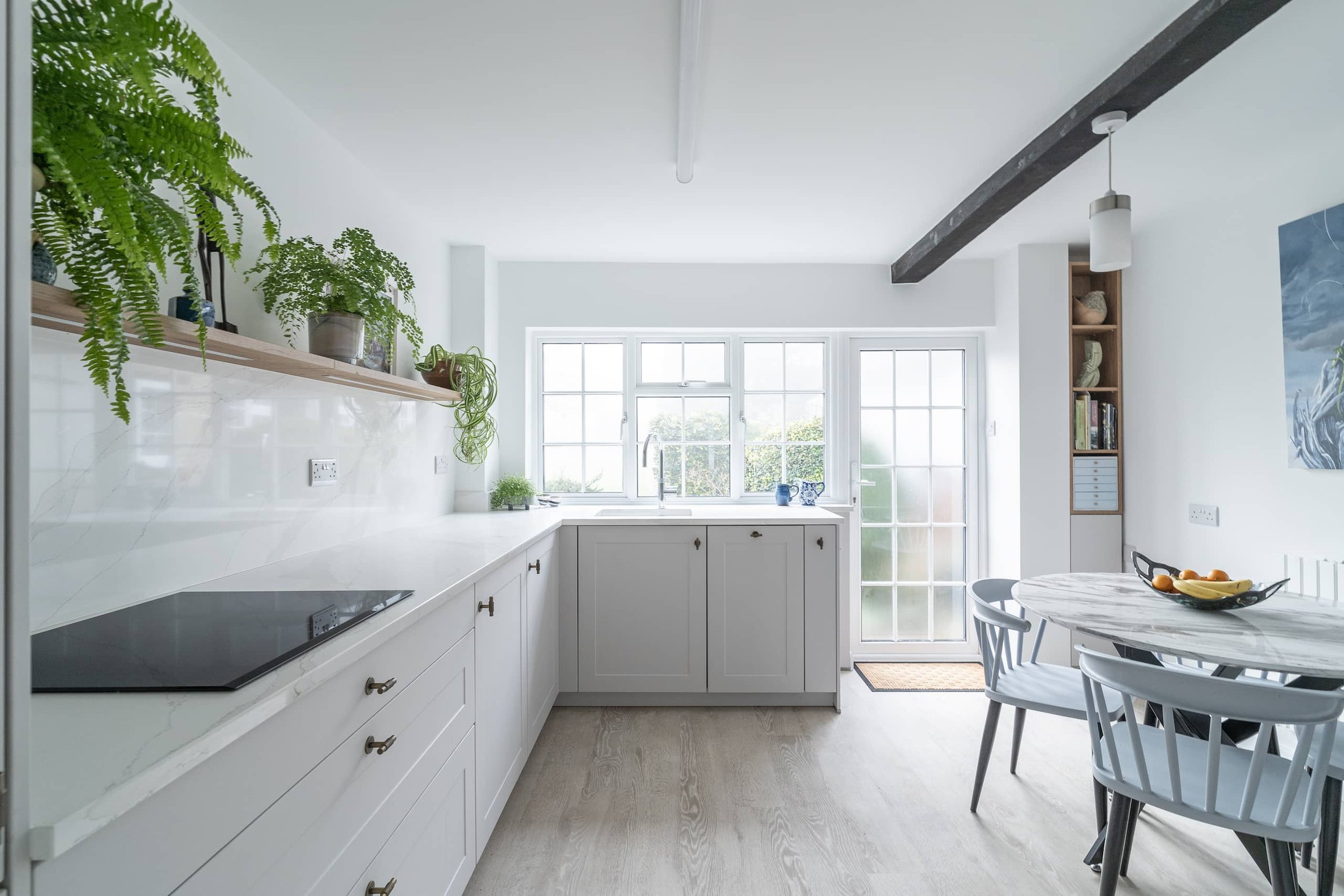 Bright kitchen with white cabinets, hanging plants, and a round marble dining table.