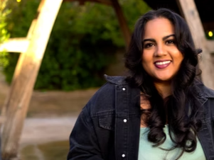 Smiling woman with dark hair and a black jacket outdoors in a park.