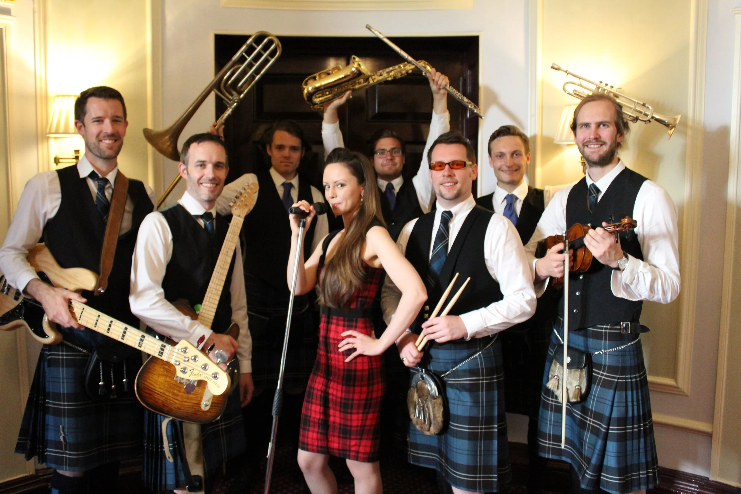 Group of musicians in formal attire, holding musical instruments, posing in a room with warm lighting.