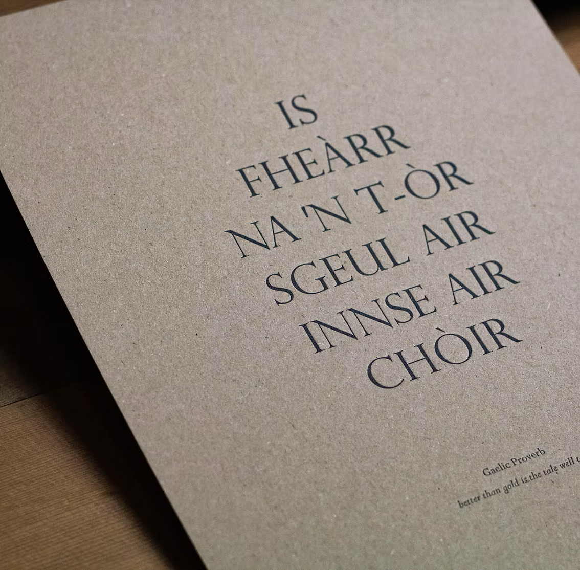 A printed page with a Gaelic proverb about the value of gold over copper, with the words: 'IS FHÈARR NAN T-OR SGS EUL AIR INNSE AIR CHÒIR' in large, black font on a textured beige background.